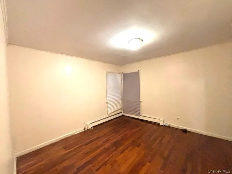 Empty room with dark wood-style floors and a baseboard heating unit Empty room with dark wood-style floors and a baseboard heating unit