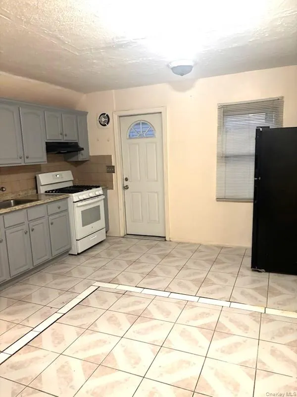 Kitchen with white gas stove, a textured ceiling, light tile patterned floors, decorative backsplash, and freestanding refrigerator Kitchen with white gas stove, a textured ceiling, light tile patterned floors, decorative backsplash, and freestanding refrigerator