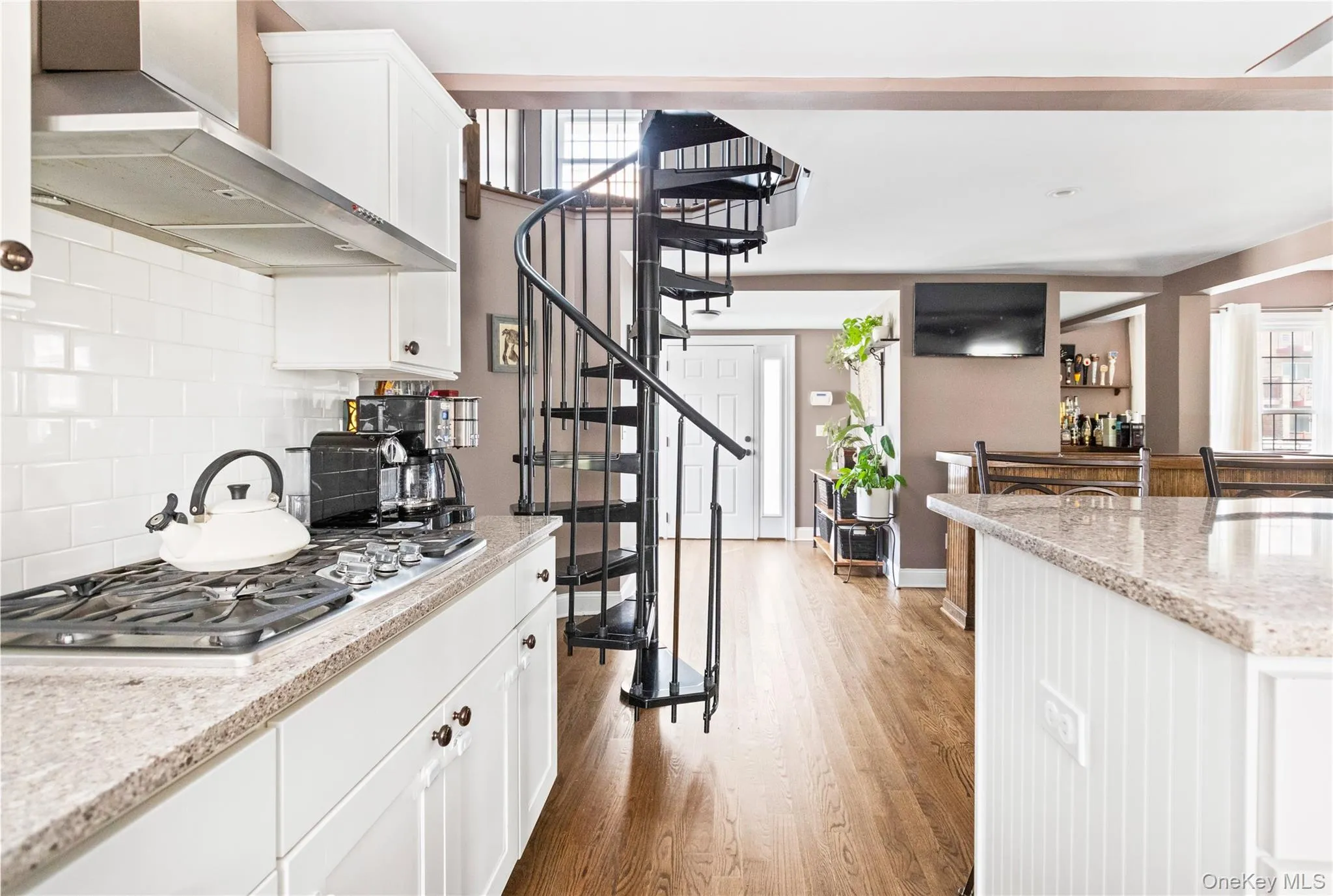 Kitchen featuring wall chimney exhaust hood, white cabinetry, plenty of natural light, and light wood-style flooring Kitchen featuring wall chimney exhaust hood, white cabinetry, plenty of natural light, and light wood-style flooring