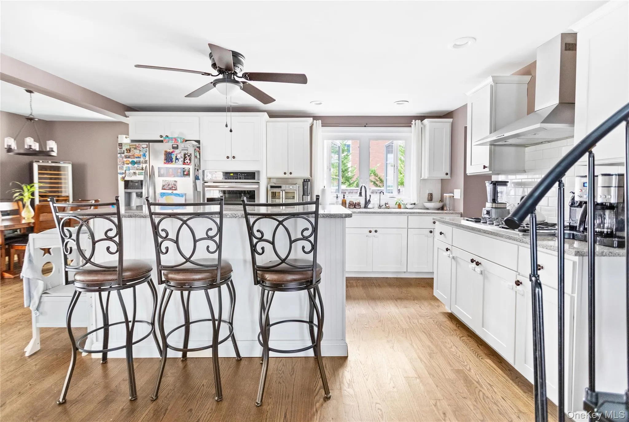 Kitchen with a breakfast bar area, a center island, white cabinetry, wall chimney range hood, and recessed lighting Kitchen with a breakfast bar area, a center island, white cabinetry, wall chimney range hood, and recessed lighting