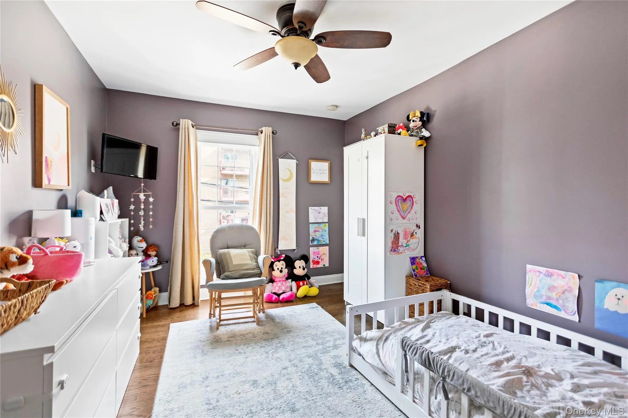 Bedroom with wood finished floors, a nursery area, and a ceiling fan Bedroom with wood finished floors, a nursery area, and a ceiling fan