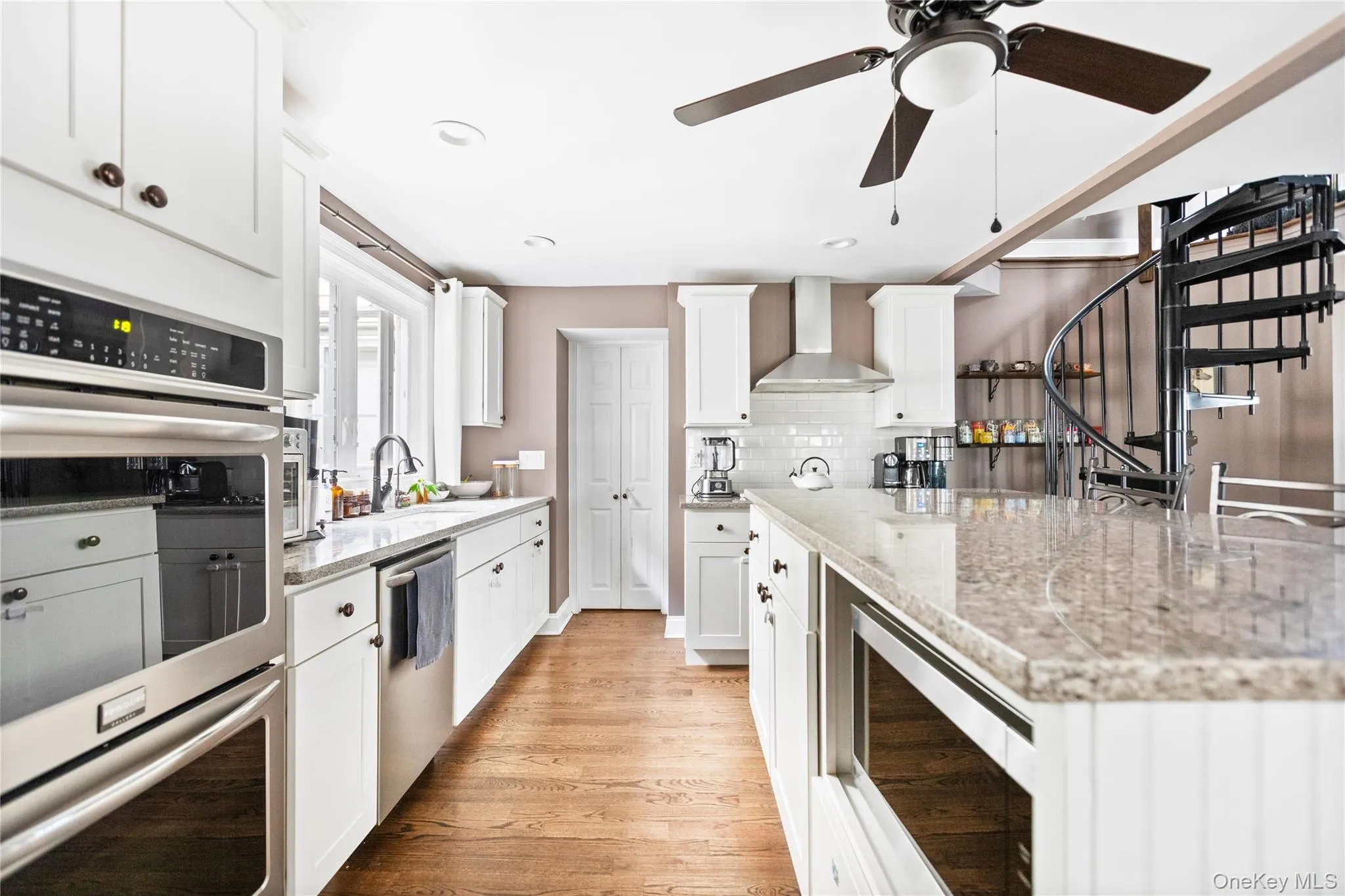 Kitchen with stainless steel appliances, white cabinets, light wood-style floors, light stone countertops, and decorative backsplash Kitchen with stainless steel appliances, white cabinets, light wood-style floors, light stone countertops, and decorative backsplash