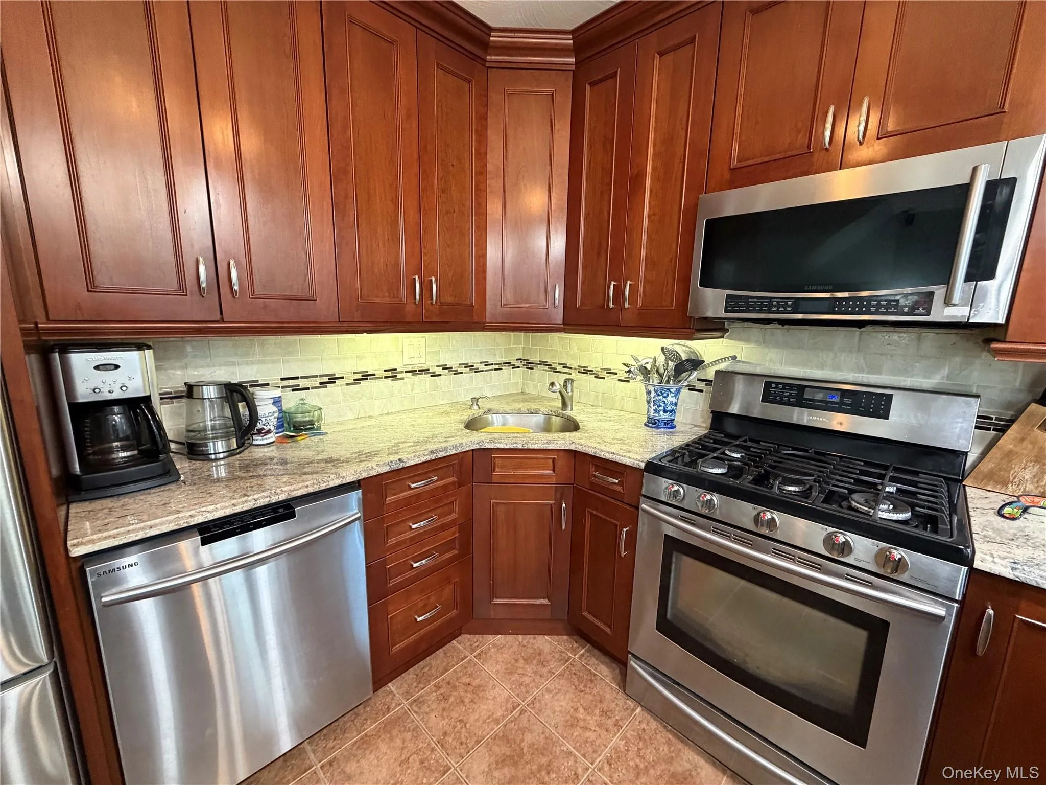Kitchen with appliances with stainless steel finishes, decorative backsplash, light tile patterned floors, and light stone countertops Kitchen with appliances with stainless steel finishes, decorative backsplash, light tile patterned floors, and light stone countertops