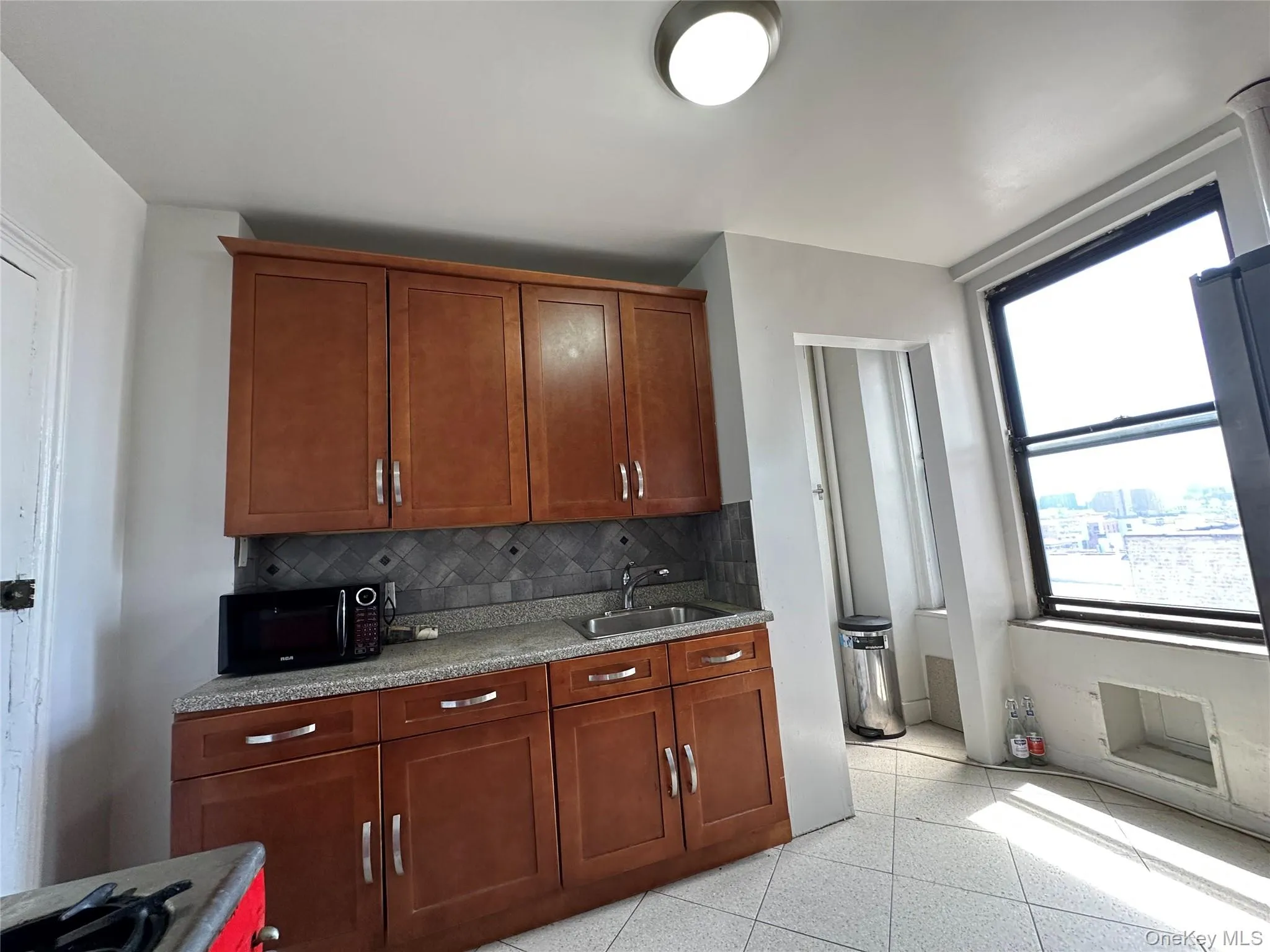 Kitchen with black microwave, a sink, backsplash, light stone counters, and brown cabinets Kitchen with black microwave, a sink, backsplash, light stone counters, and brown cabinets