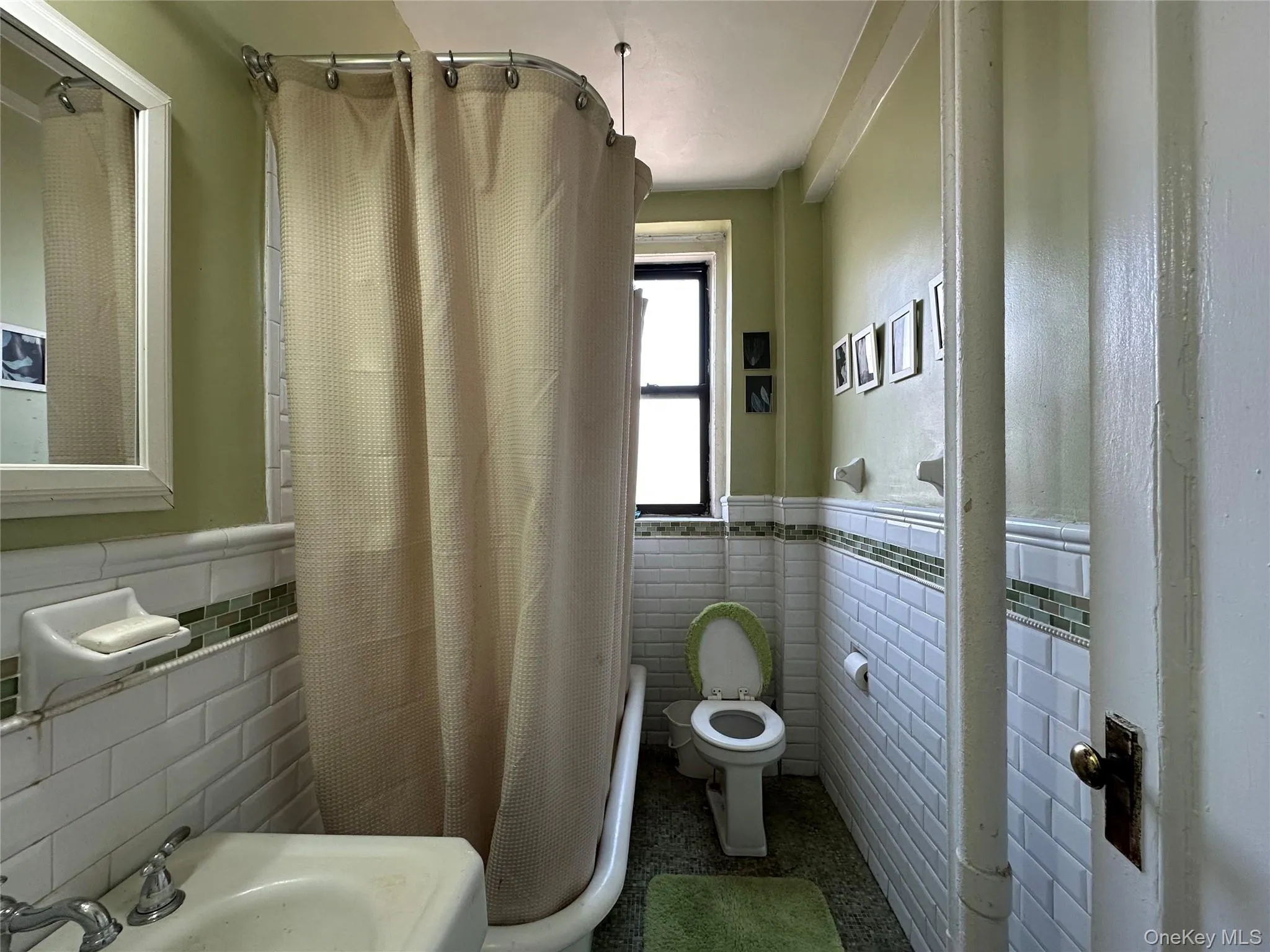 Full bath featuring tile walls, a sink, a wainscoted wall, and toilet Full bath featuring tile walls, a sink, a wainscoted wall, and toilet