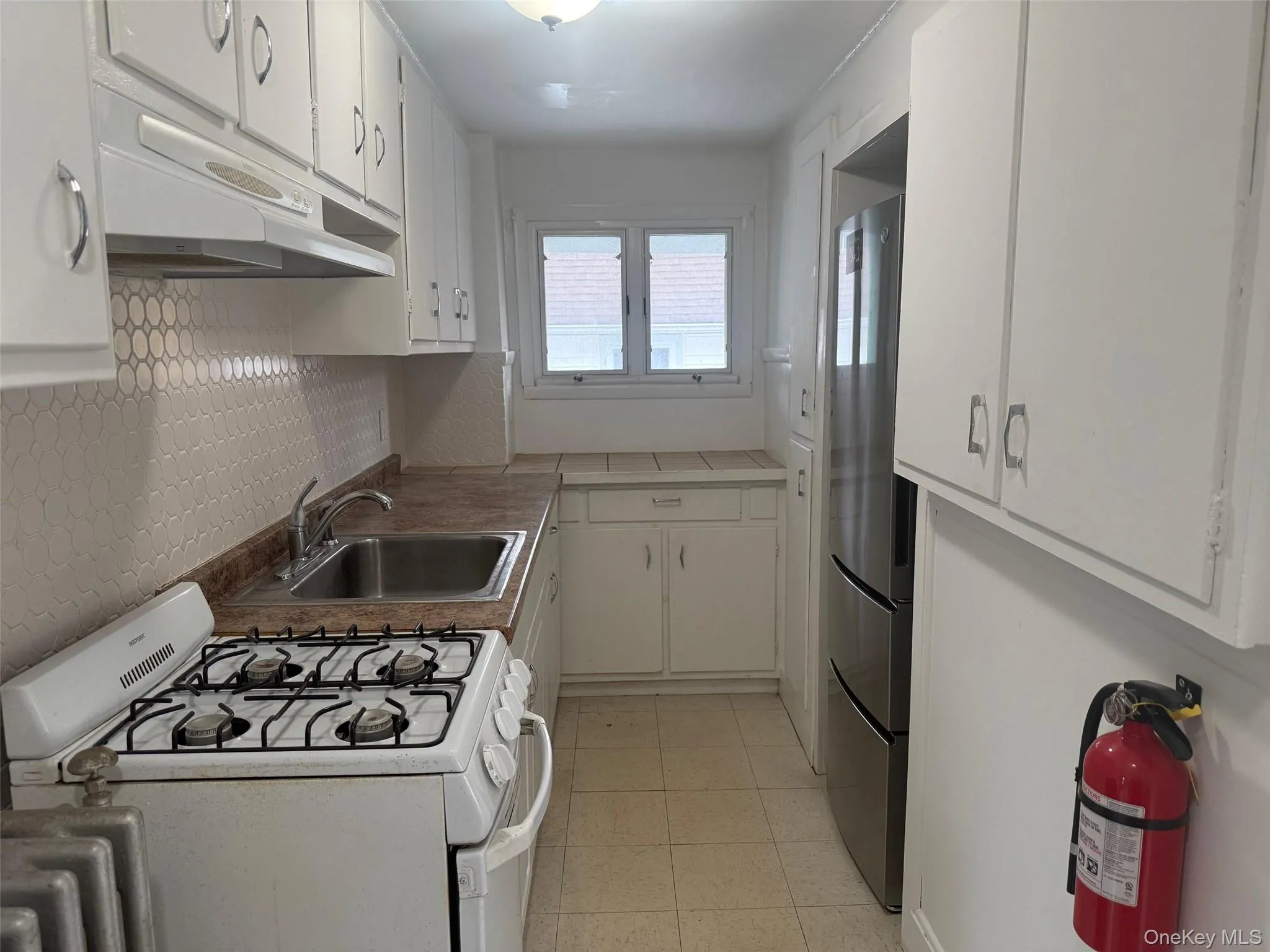 Kitchen with white gas range oven, white cabinets, under cabinet range hood, freestanding refrigerator, and light tile patterned flooring Kitchen with white gas range oven, white cabinets, under cabinet range hood, freestanding refrigerator, and light tile patterned flooring