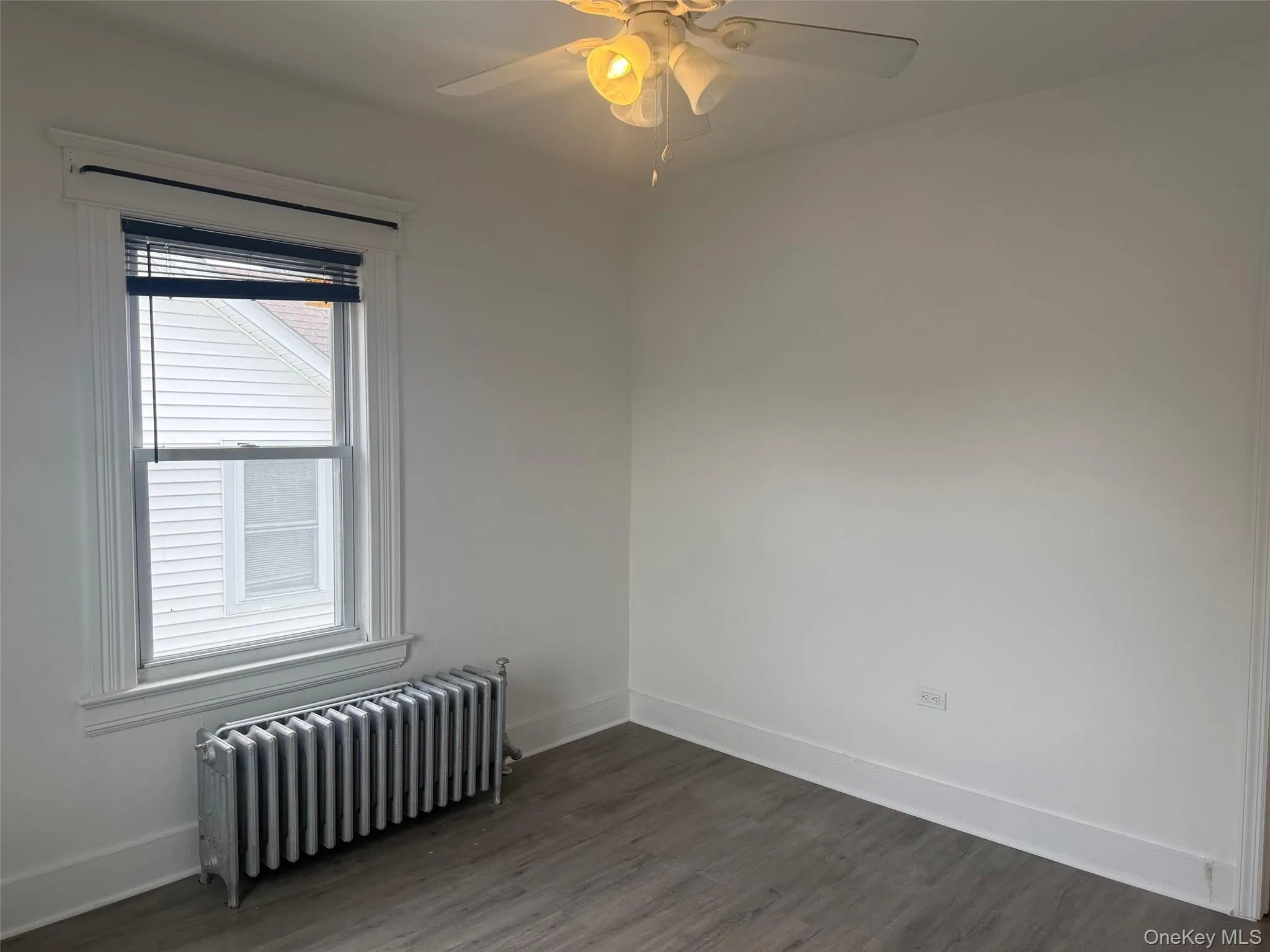 Empty room can be used for office with radiator heating unit, dark wood-style flooring, and a ceiling fan Empty room can be used for office with radiator heating unit, dark wood-style flooring, and a ceiling fan