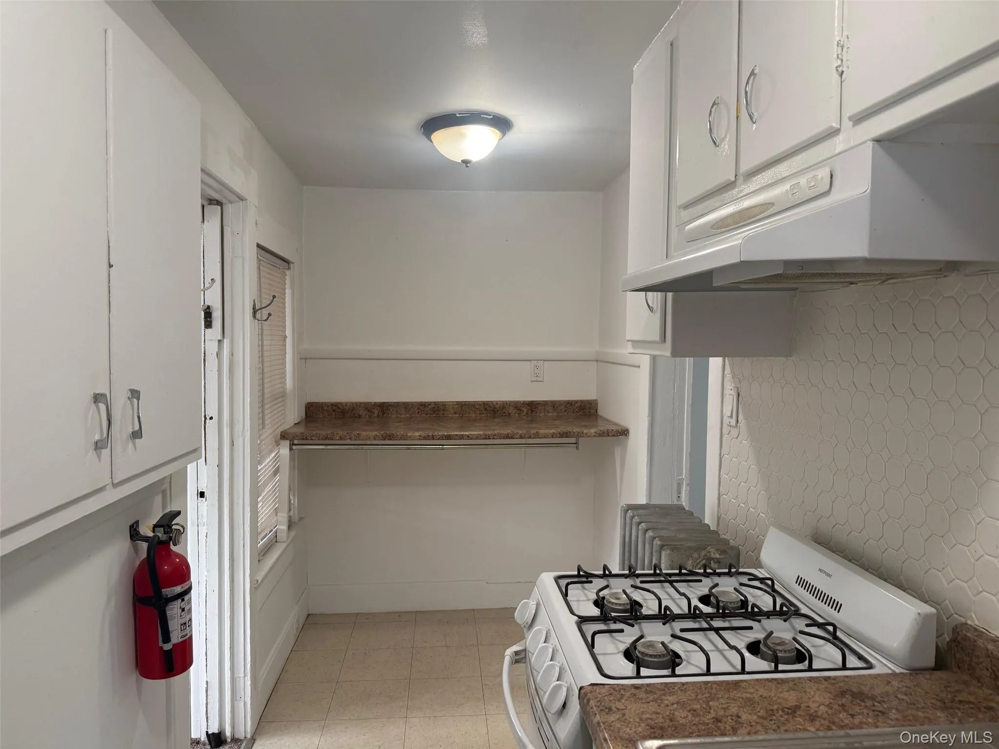 Kitchen with white range with gas stovetop, white cabinets, under cabinet range hood, tasteful backsplash, and dark countertops Kitchen with white range with gas stovetop, white cabinets, under cabinet range hood, tasteful backsplash, and dark countertops