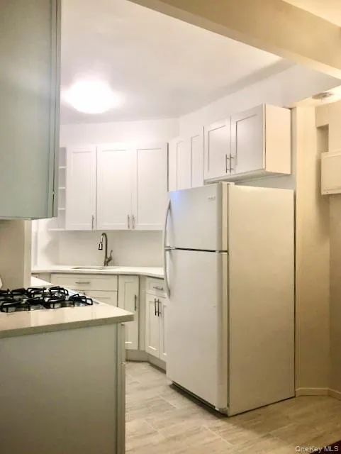Kitchen with freestanding refrigerator, white cabinets, light wood-style floors, and stainless steel gas stovetop Kitchen with freestanding refrigerator, white cabinets, light wood-style floors, and stainless steel gas stovetop