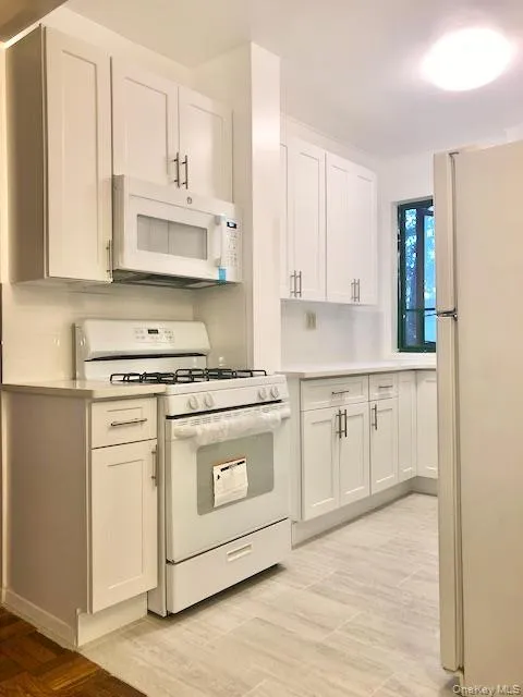 Kitchen with white appliances, white cabinets, light countertops, and light wood-type flooring Kitchen with white appliances, white cabinets, light countertops, and light wood-type flooring