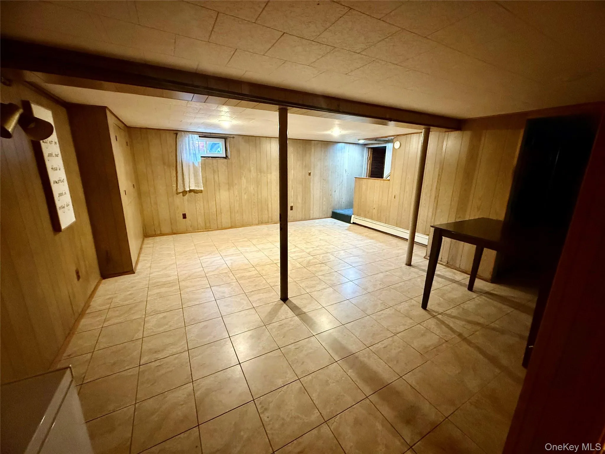 Basement with wood walls, baseboard heating, and light tile patterned floors Basement with wood walls, baseboard heating, and light tile patterned floors