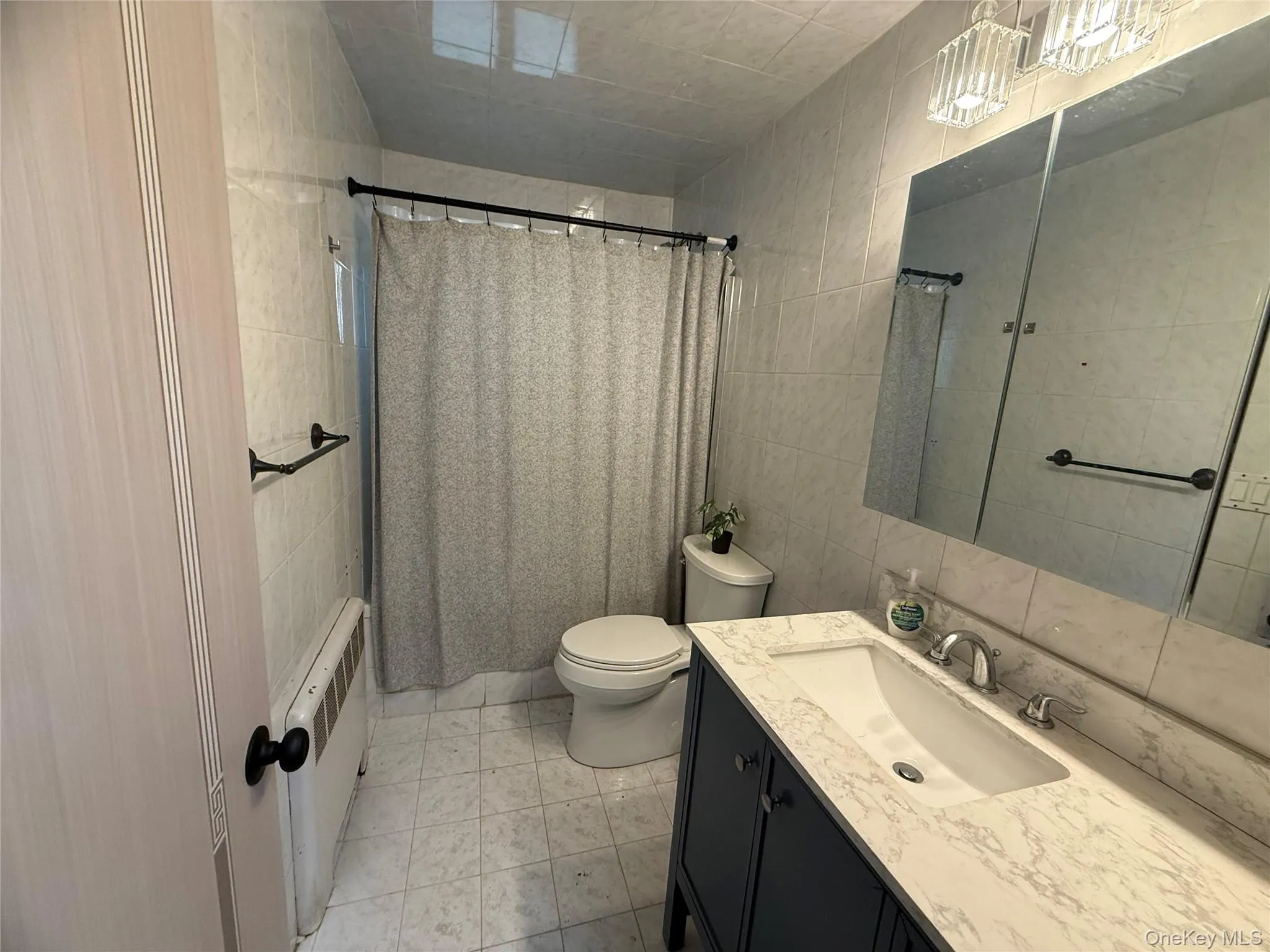 Bathroom featuring tile walls, radiator heating unit, vanity, light tile patterned flooring, and shower / tub combo with curtain on the 1st fl Bathroom featuring tile walls, radiator heating unit, vanity, light tile patterned flooring, and shower / tub combo with curtain on the 1st fl