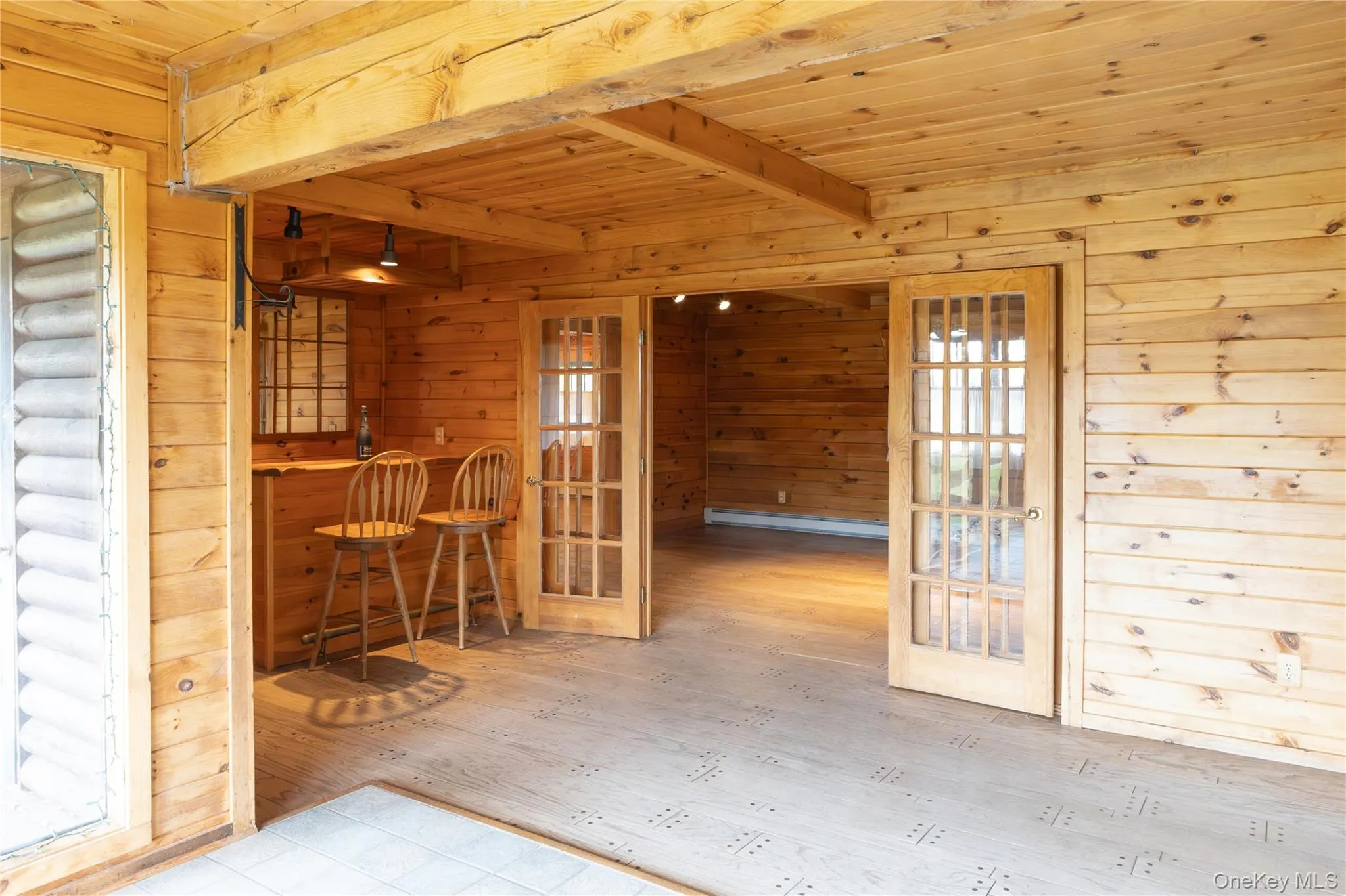Unfurnished dining area featuring a bar, a wooden ceiling with exposed beams, wooden walls, french doors, and a baseboard heating unit Unfurnished dining area featuring a bar, a wooden ceiling with exposed beams, wooden walls, french doors, and a baseboard heating unit