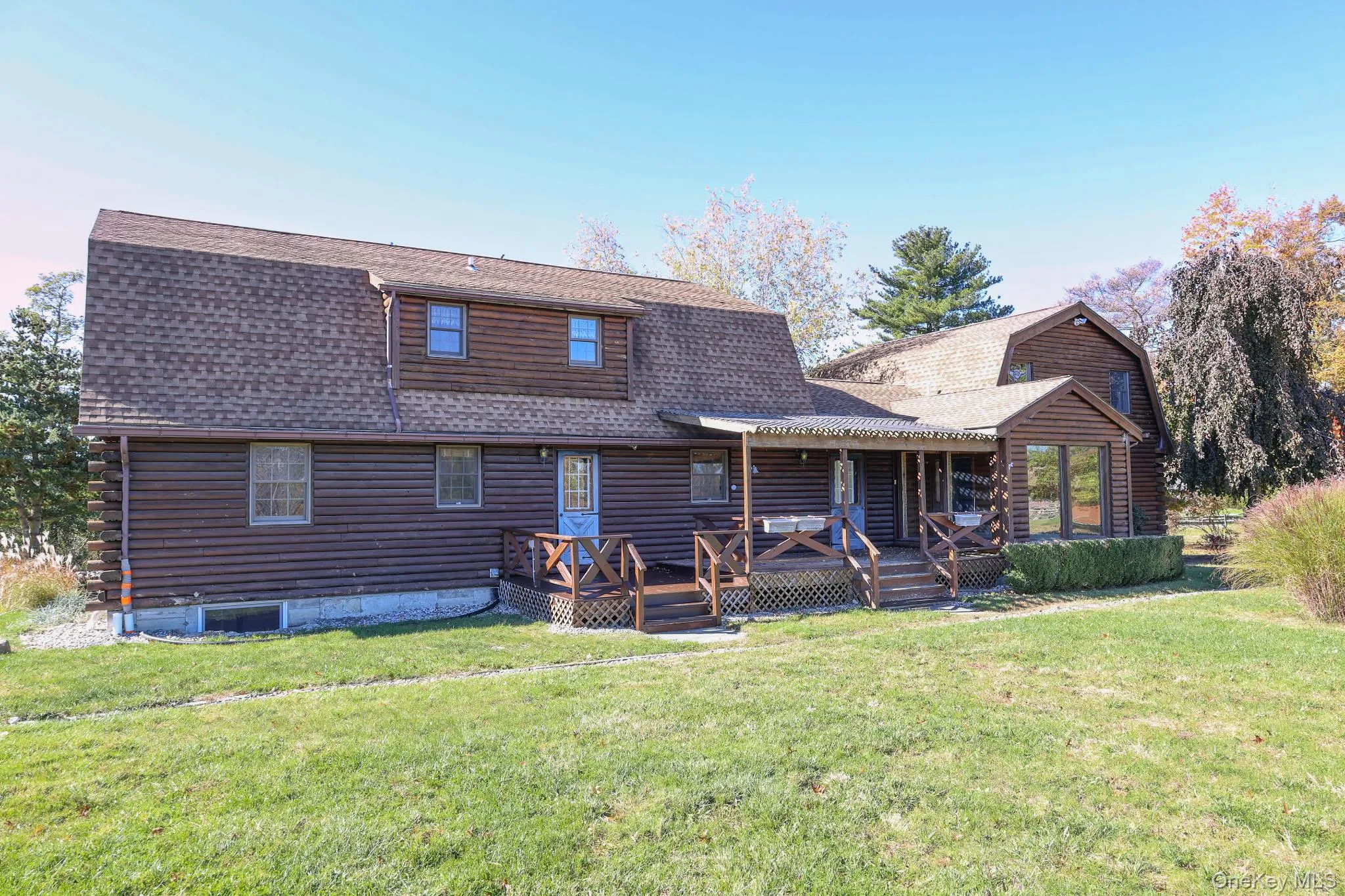 Back of house featuring a gambrel roof, a shingled roof, a yard, and log siding Back of house featuring a gambrel roof, a shingled roof, a yard, and log siding
