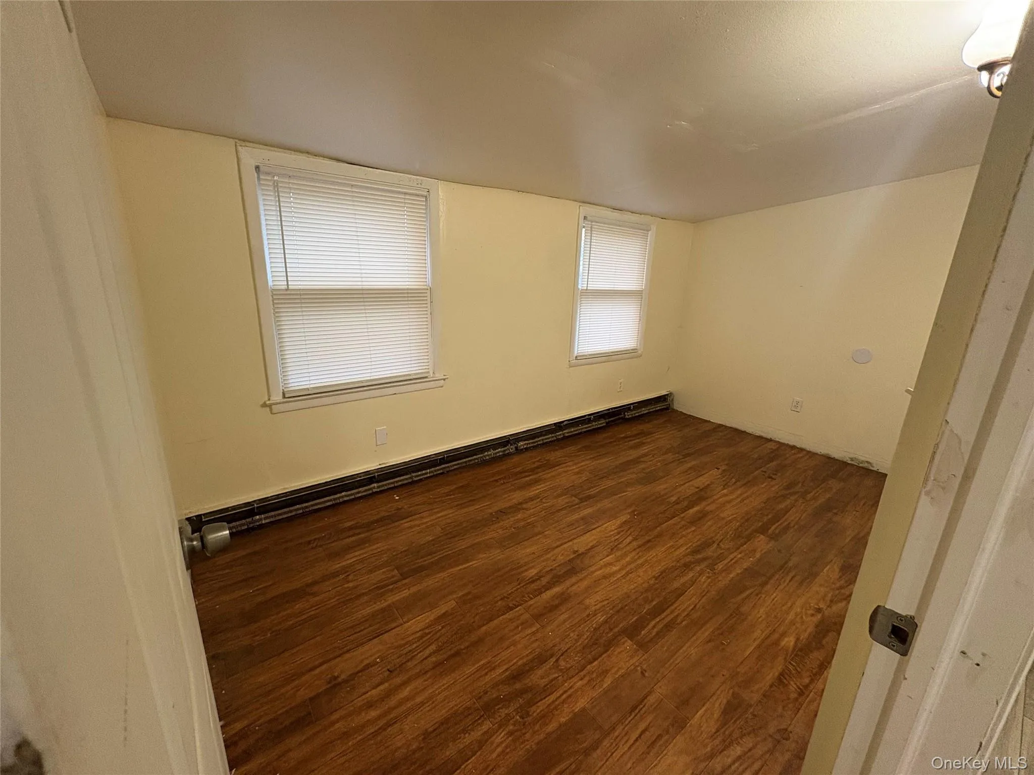 Empty room with a baseboard heating unit and dark wood finished floors Empty room with a baseboard heating unit and dark wood finished floors