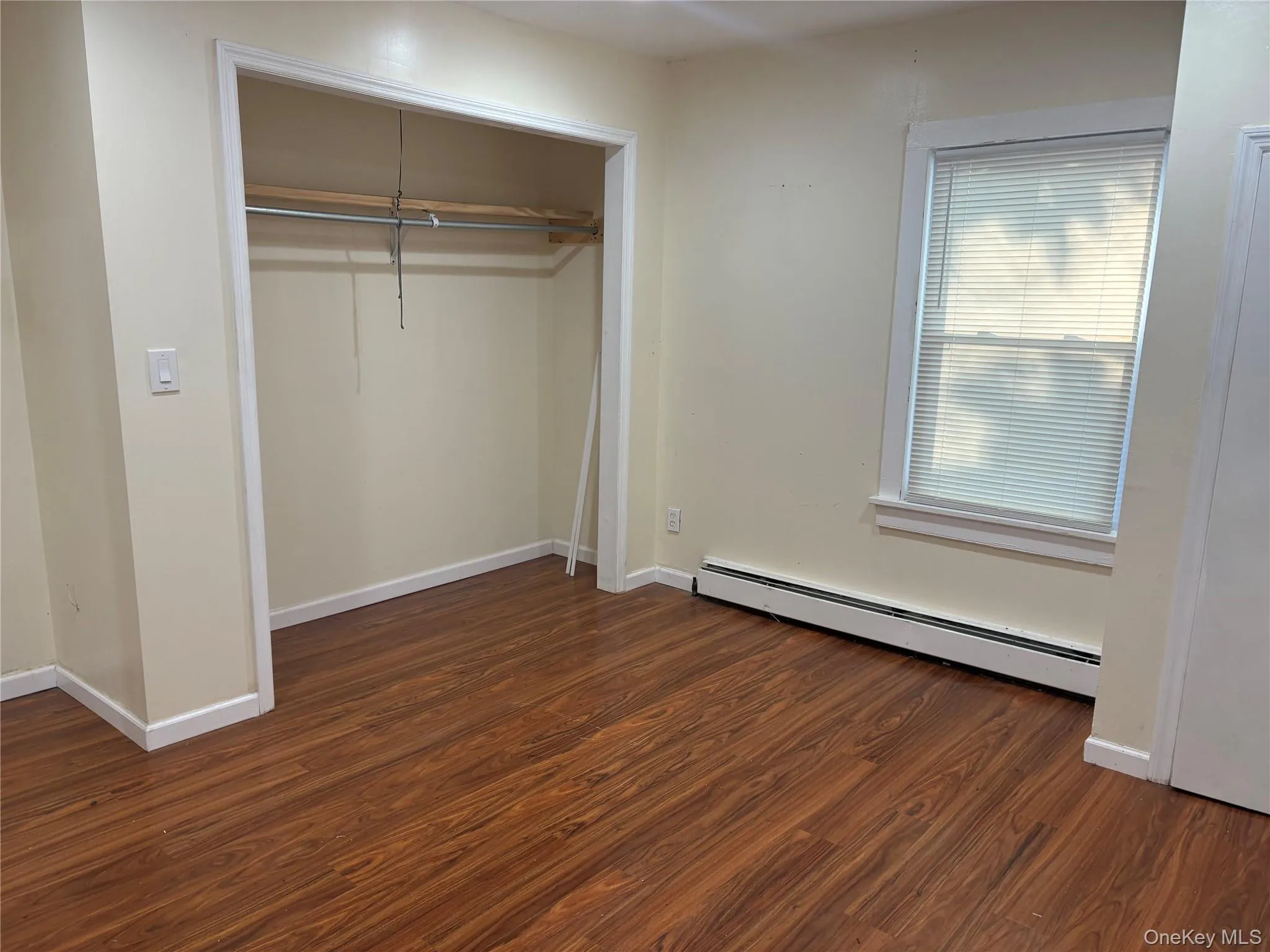 Unfurnished bedroom featuring a baseboard radiator, dark wood-style floors, and a closet Unfurnished bedroom featuring a baseboard radiator, dark wood-style floors, and a closet
