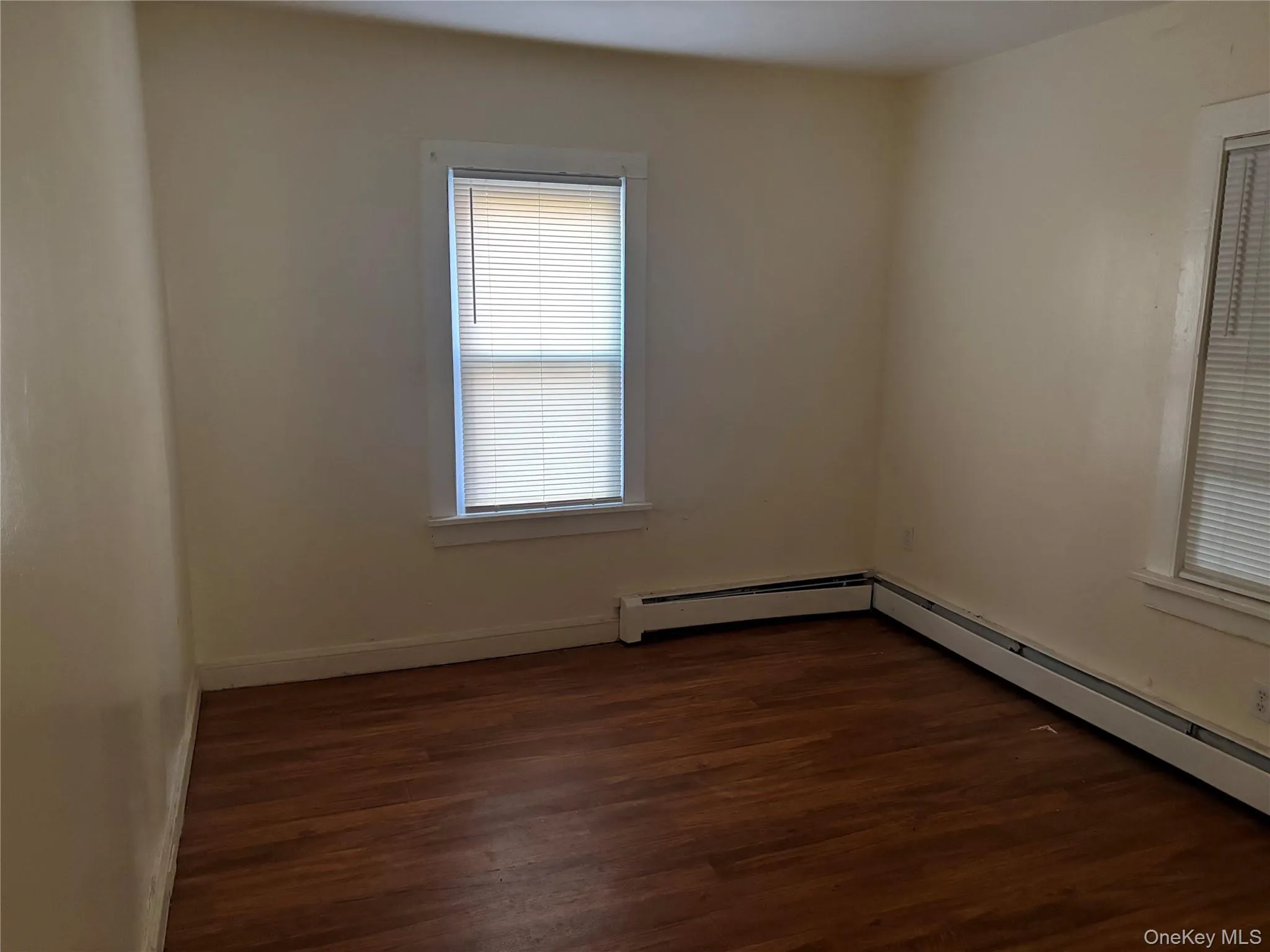 Empty room with dark wood-style floors and baseboard heating Empty room with dark wood-style floors and baseboard heating