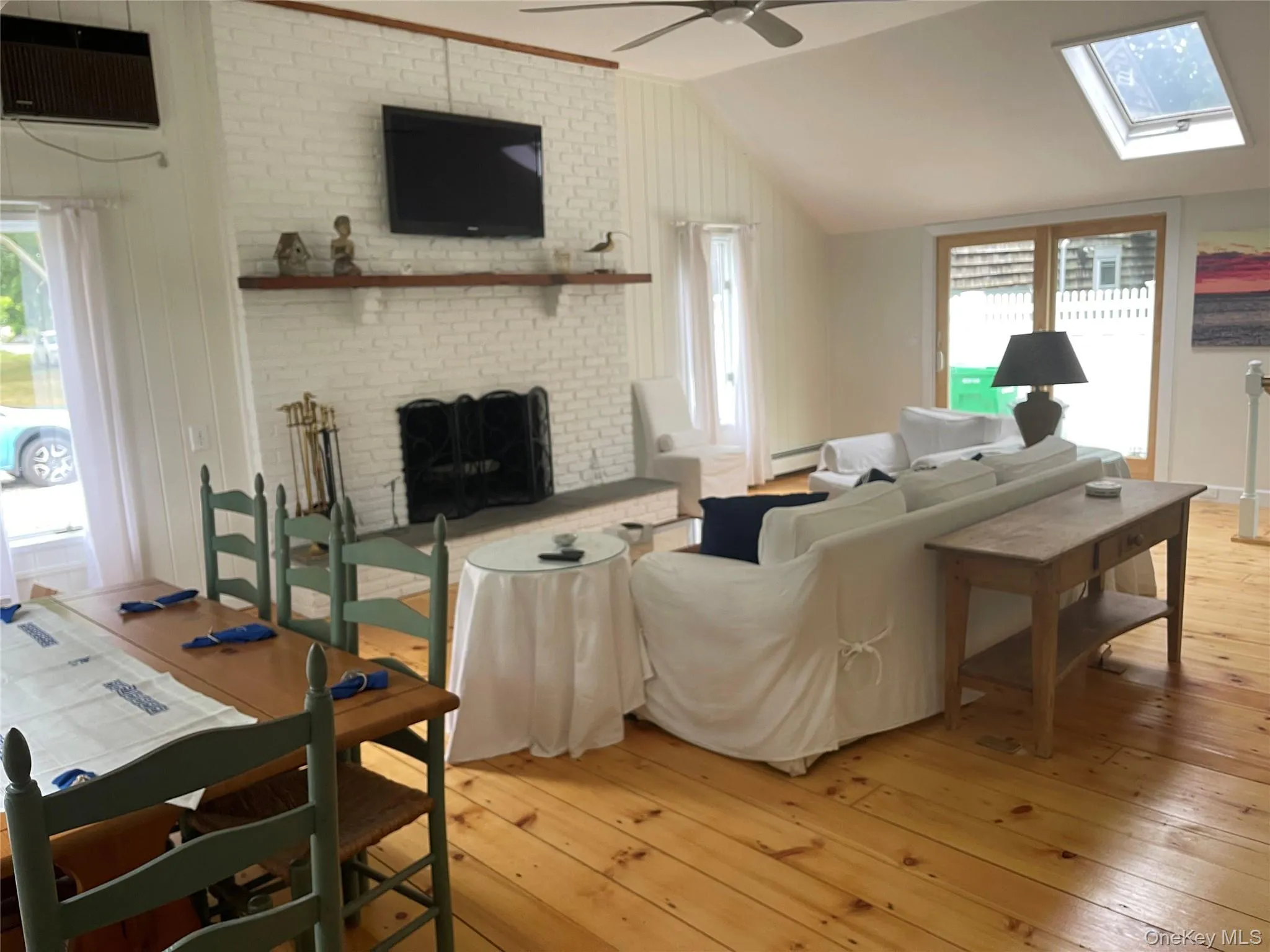 Living area featuring light wood finished floors, a brick fireplace, vaulted ceiling, a ceiling fan, and a wall unit AC Living area featuring light wood finished floors, a brick fireplace, vaulted ceiling, a ceiling fan, and a wall unit AC