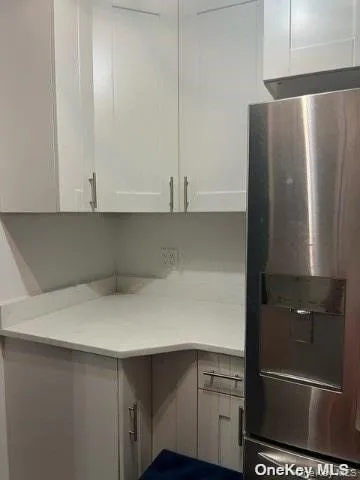 Kitchen featuring stainless steel fridge with ice dispenser, white cabinetry, and light stone countertops Kitchen featuring stainless steel fridge with ice dispenser, white cabinetry, and light stone countertops