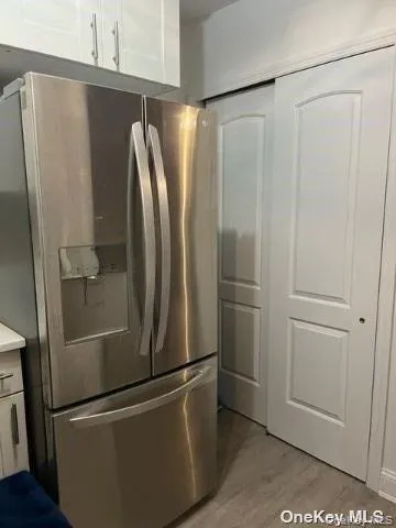 Kitchen with stainless steel refrigerator with ice dispenser, light wood finished floors, white cabinetry, and light countertops Kitchen with stainless steel refrigerator with ice dispenser, light wood finished floors, white cabinetry, and light countertops