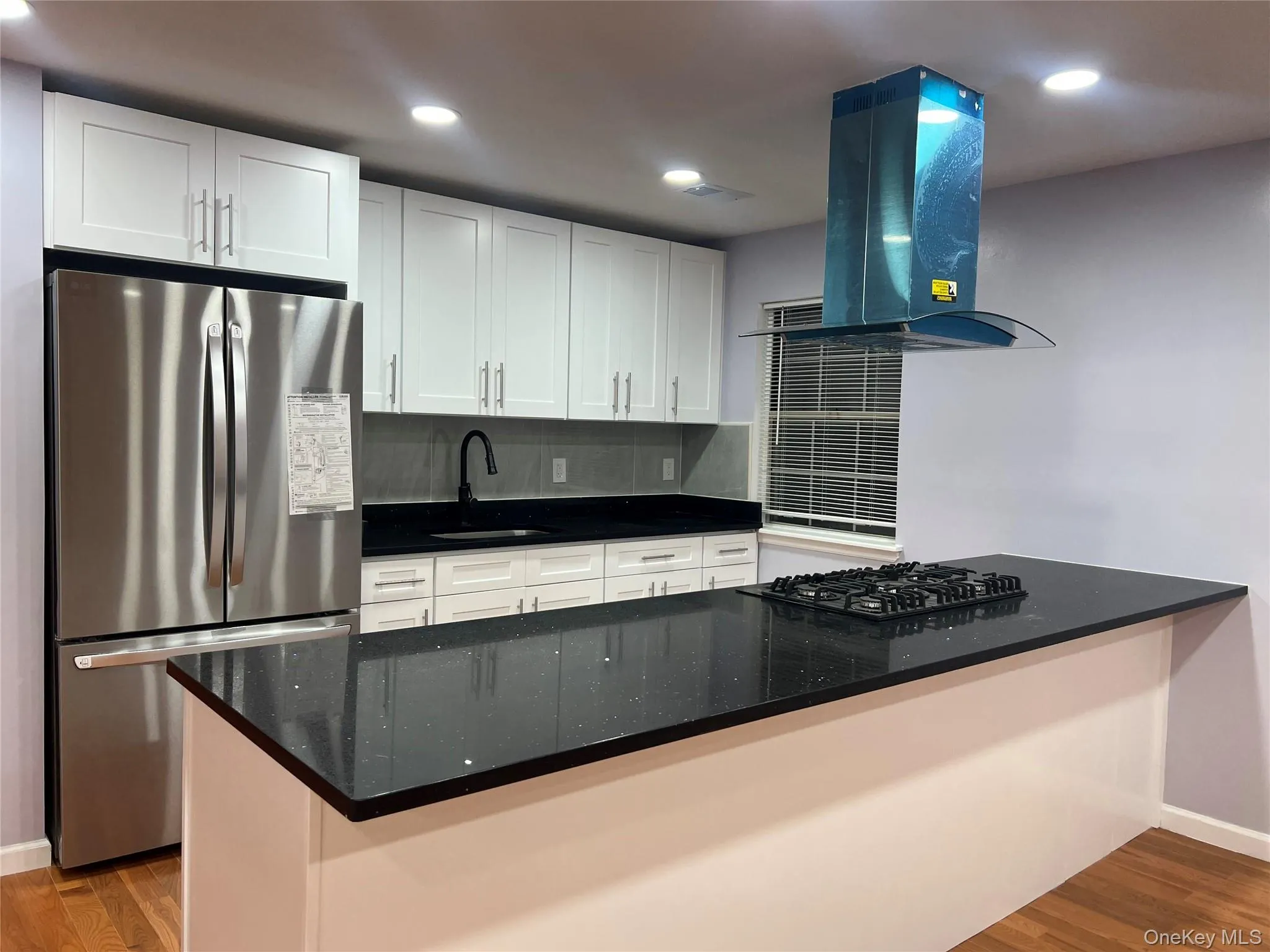 Kitchen featuring freestanding refrigerator, wood finished floors, ventilation hood, white cabinetry, and recessed lighting Kitchen featuring freestanding refrigerator, wood finished floors, ventilation hood, white cabinetry, and recessed lighting
