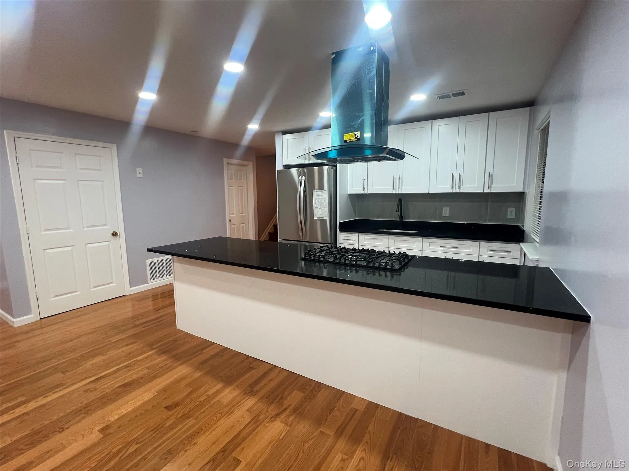 Kitchen featuring island exhaust hood, white cabinets, light wood finished floors, freestanding refrigerator, and dark countertops Kitchen featuring island exhaust hood, white cabinets, light wood finished floors, freestanding refrigerator, and dark countertops