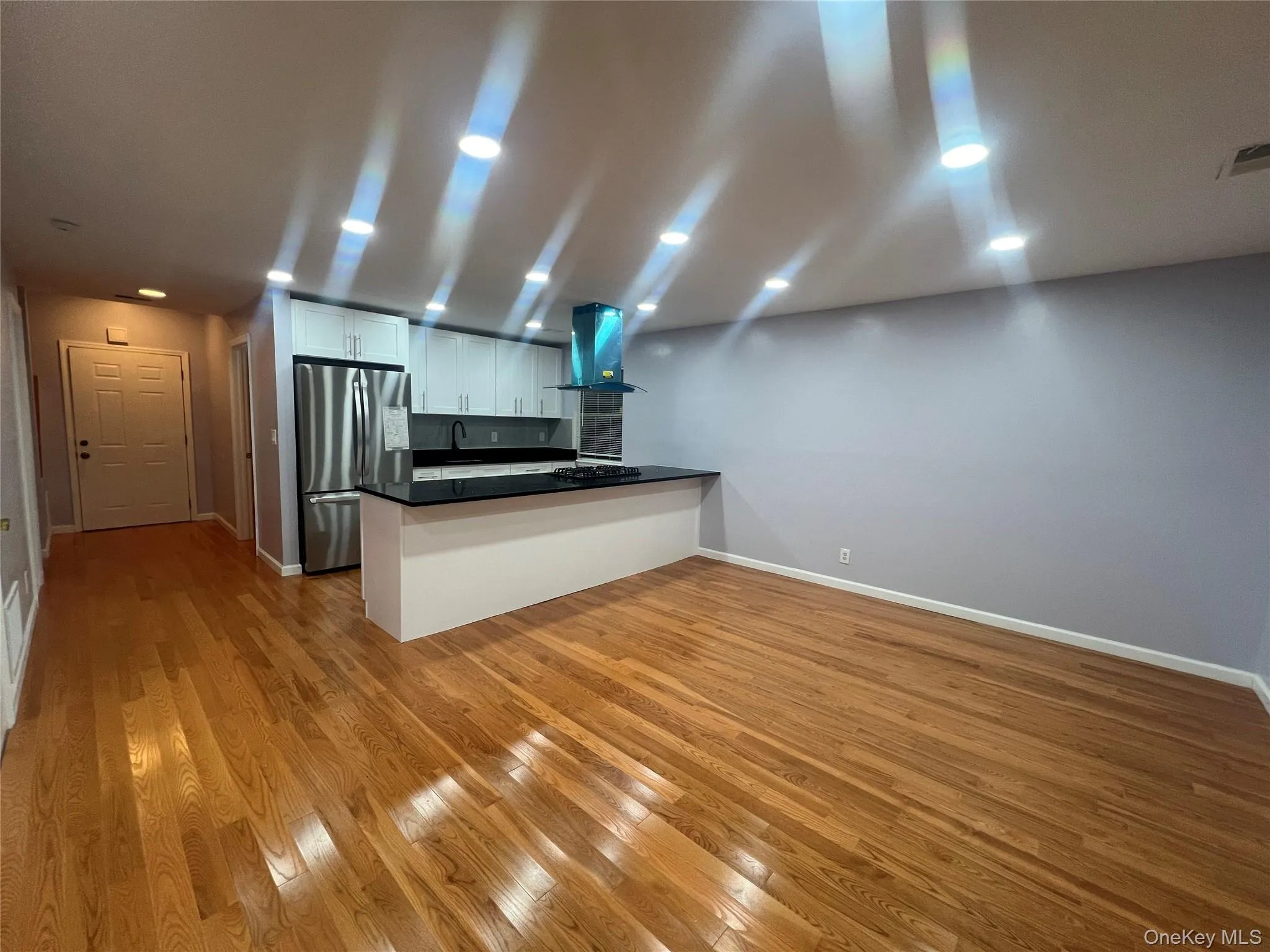 Kitchen featuring a peninsula, freestanding refrigerator, white cabinetry, light wood-type flooring, and recessed lighting Kitchen featuring a peninsula, freestanding refrigerator, white cabinetry, light wood-type flooring, and recessed lighting