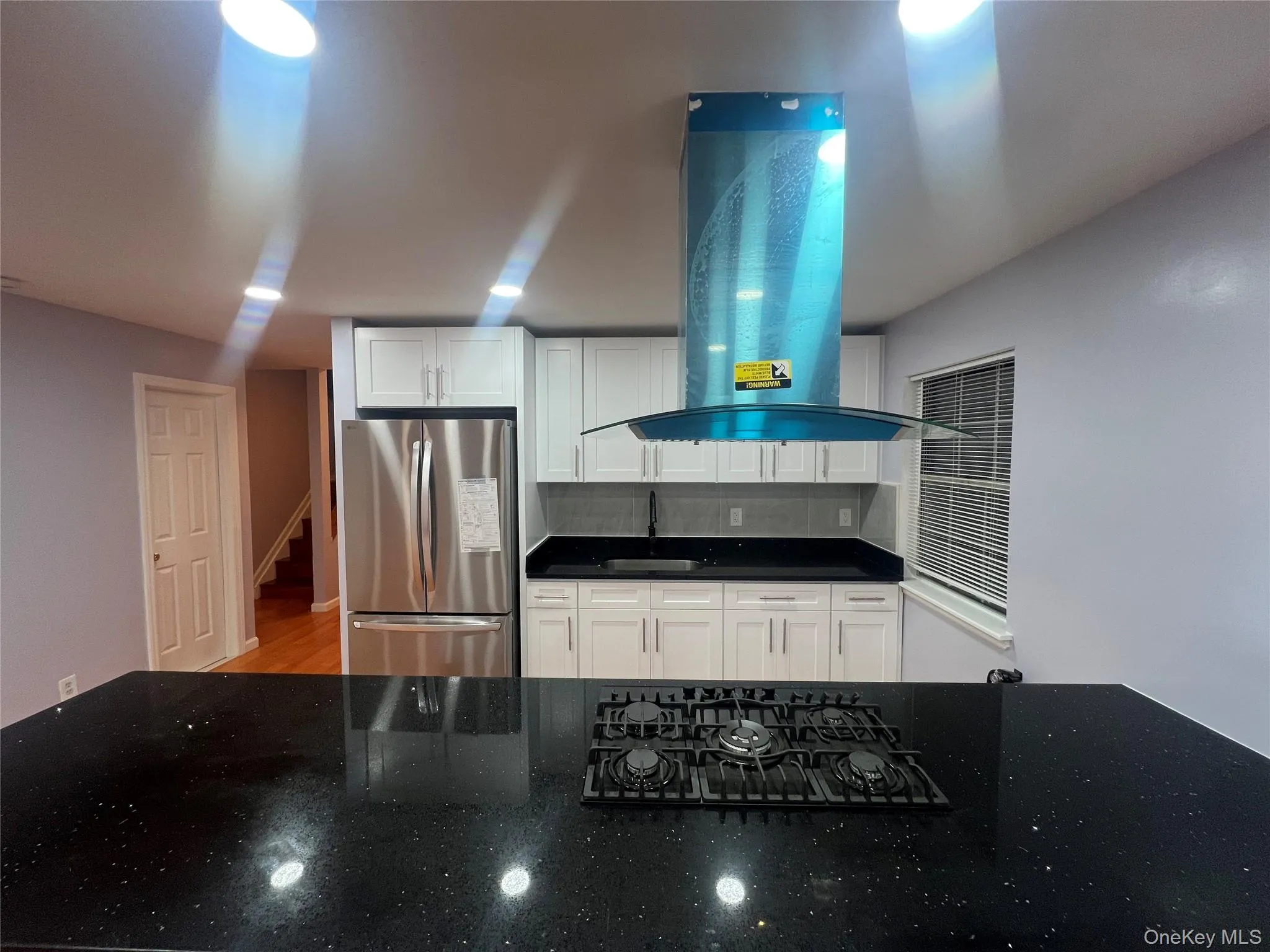Kitchen featuring exhaust hood, freestanding refrigerator, black gas stovetop, white cabinetry, and dark stone countertops Kitchen featuring exhaust hood, freestanding refrigerator, black gas stovetop, white cabinetry, and dark stone countertops