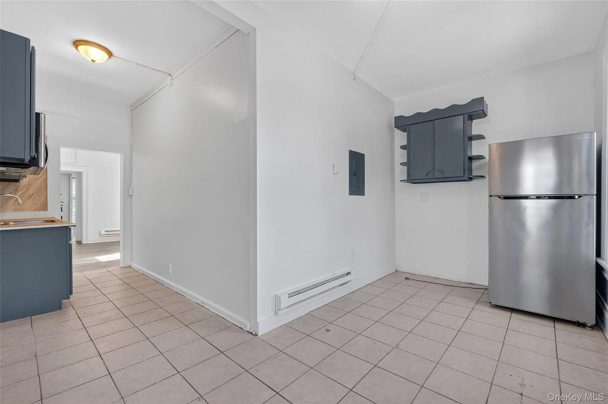 Kitchen with freestanding refrigerator, open shelves, light tile patterned flooring, a baseboard radiator, and electric panel Kitchen with freestanding refrigerator, open shelves, light tile patterned flooring, a baseboard radiator, and electric panel