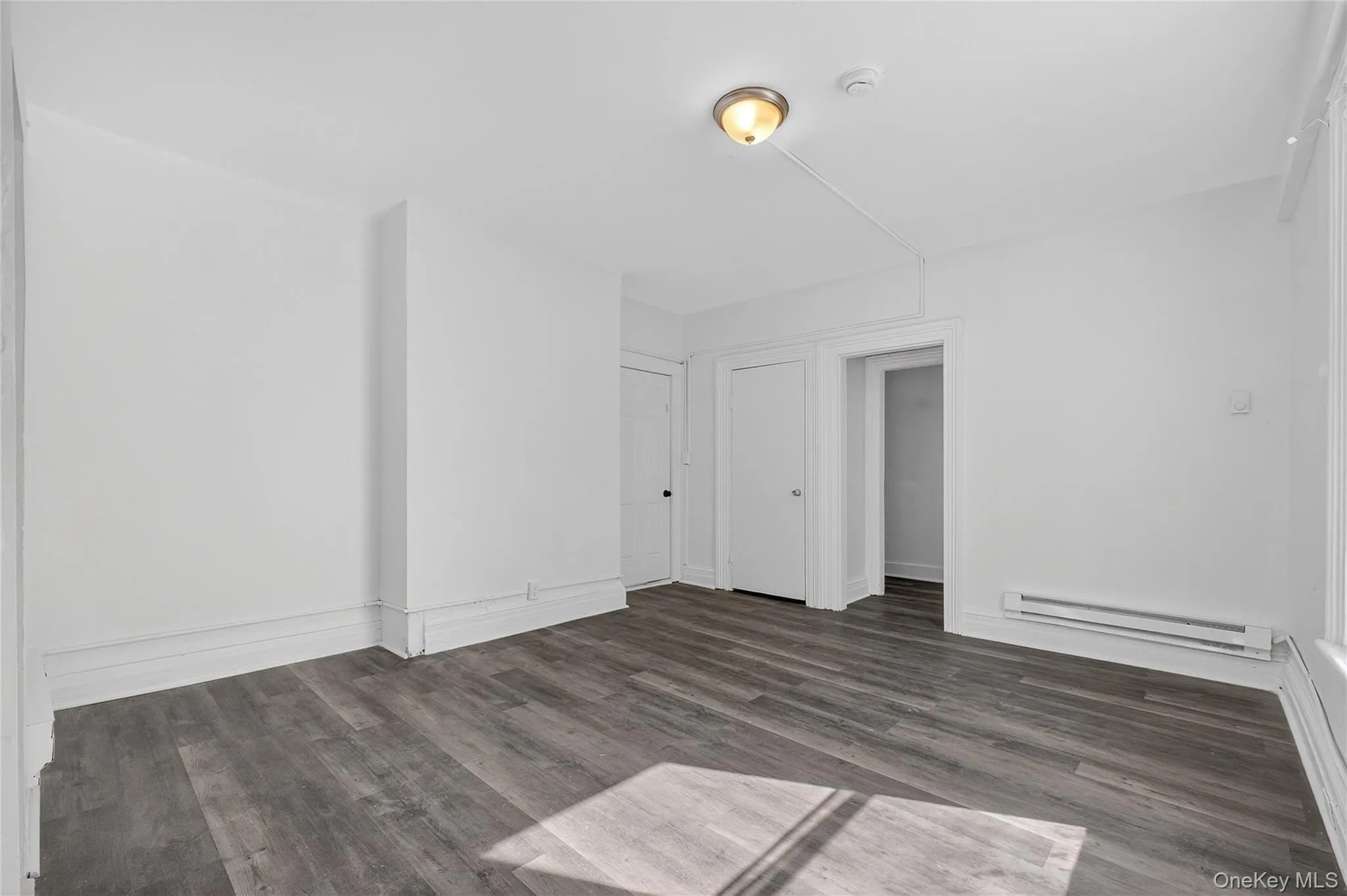 Unfurnished room with dark wood finished floors and a baseboard heating unit Unfurnished room with dark wood finished floors and a baseboard heating unit