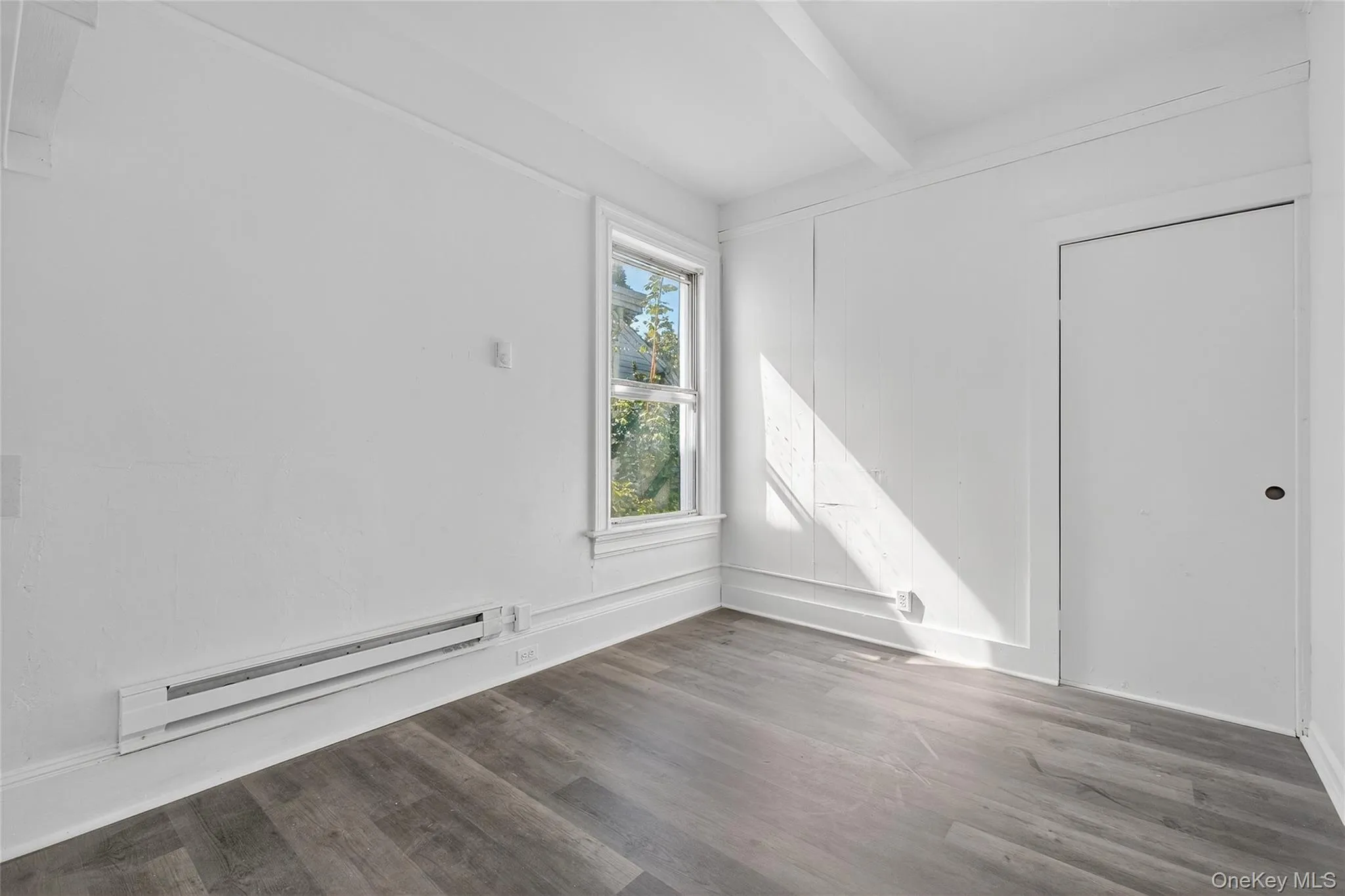 Unfurnished room with a baseboard heating unit, wood finished floors, and beam ceiling Unfurnished room with a baseboard heating unit, wood finished floors, and beam ceiling
