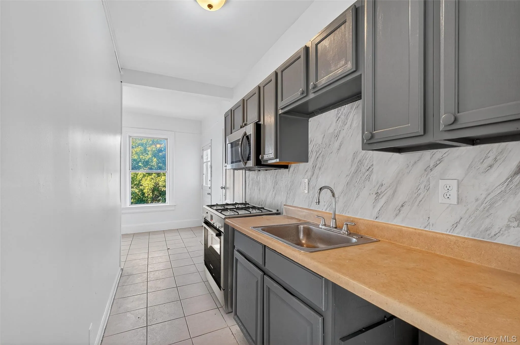Kitchen with stainless steel appliances, light tile patterned floors, light countertops, tasteful backsplash, and gray cabinets Kitchen with stainless steel appliances, light tile patterned floors, light countertops, tasteful backsplash, and gray cabinets