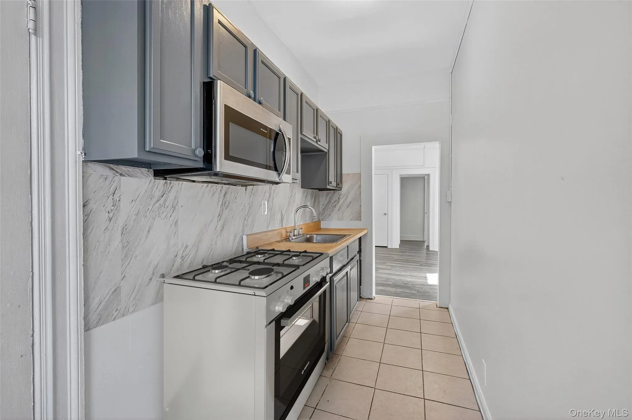 Kitchen featuring white gas range, light tile patterned flooring, tasteful backsplash, stainless steel microwave, and gray cabinetry Kitchen featuring white gas range, light tile patterned flooring, tasteful backsplash, stainless steel microwave, and gray cabinetry