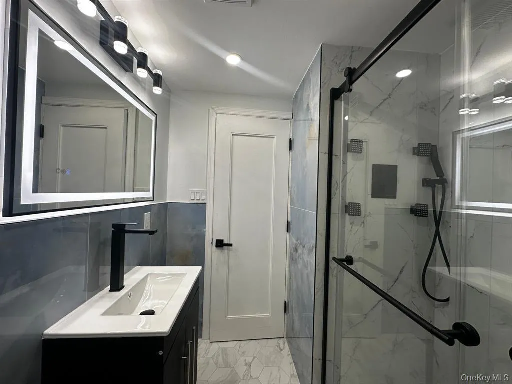 Full bath with vanity, a marble finish shower, tile walls, and light marble finish floors Full bath with vanity, a marble finish shower, tile walls, and light marble finish floors
