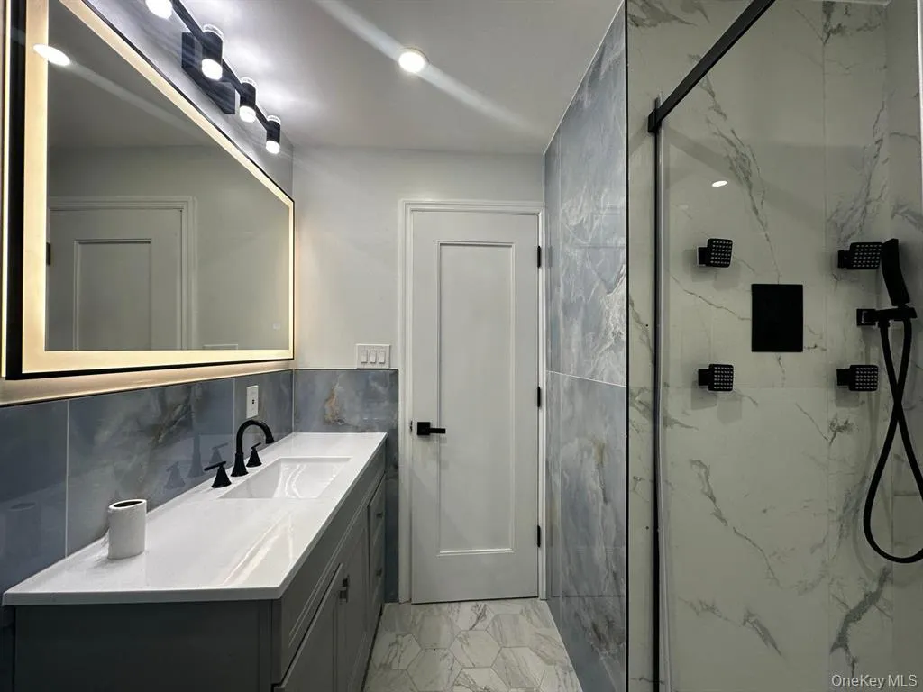 Full bath featuring vanity, light marble finish flooring, a marble finish shower, and tile walls Full bath featuring vanity, light marble finish flooring, a marble finish shower, and tile walls