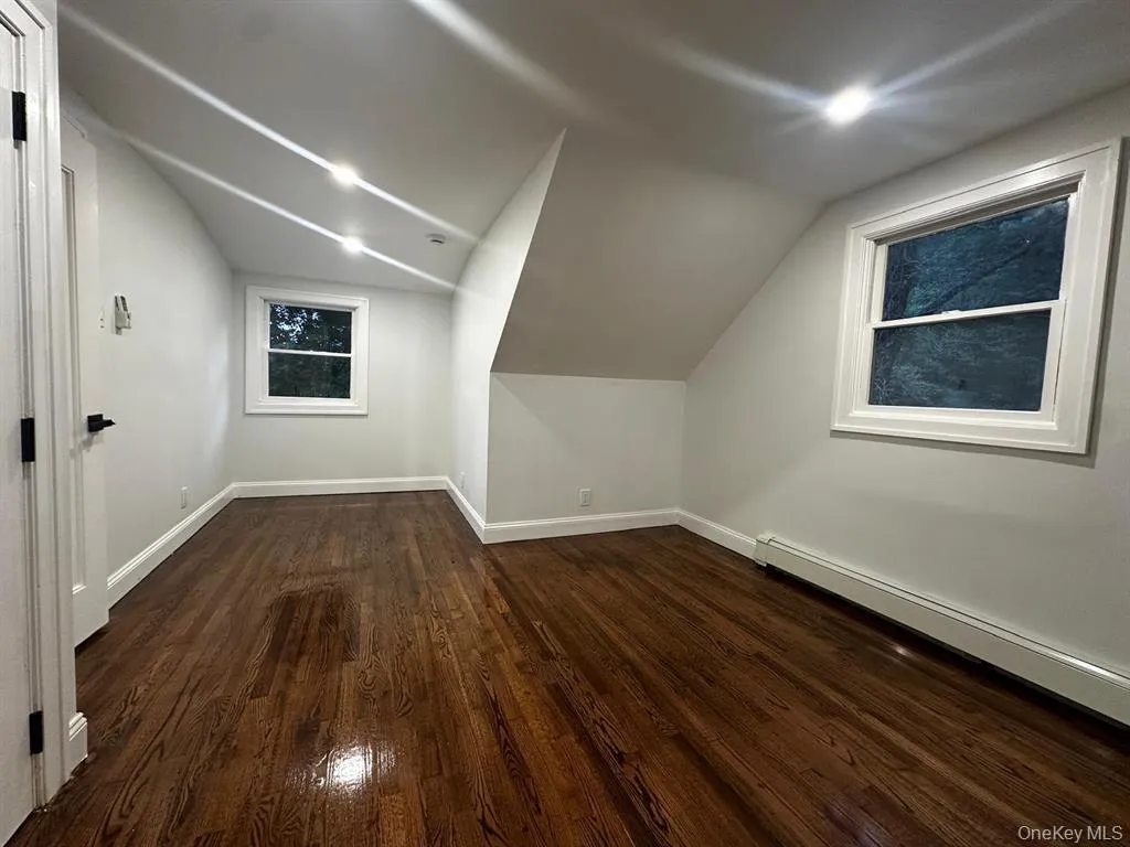 Additional living space featuring dark wood finished floors, lofted ceiling, and baseboard heating Additional living space featuring dark wood finished floors, lofted ceiling, and baseboard heating