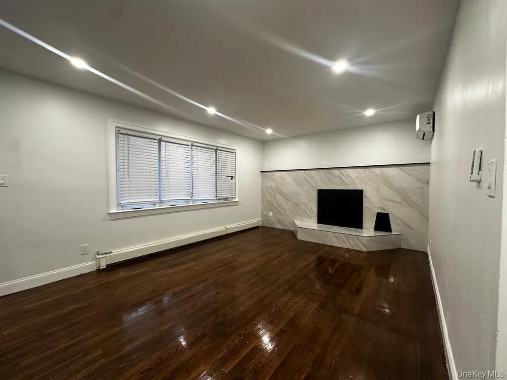 Unfurnished living room featuring a baseboard heating unit, dark wood-type flooring, a wall unit AC, and recessed lighting Unfurnished living room featuring a baseboard heating unit, dark wood-type flooring, a wall unit AC, and recessed lighting
