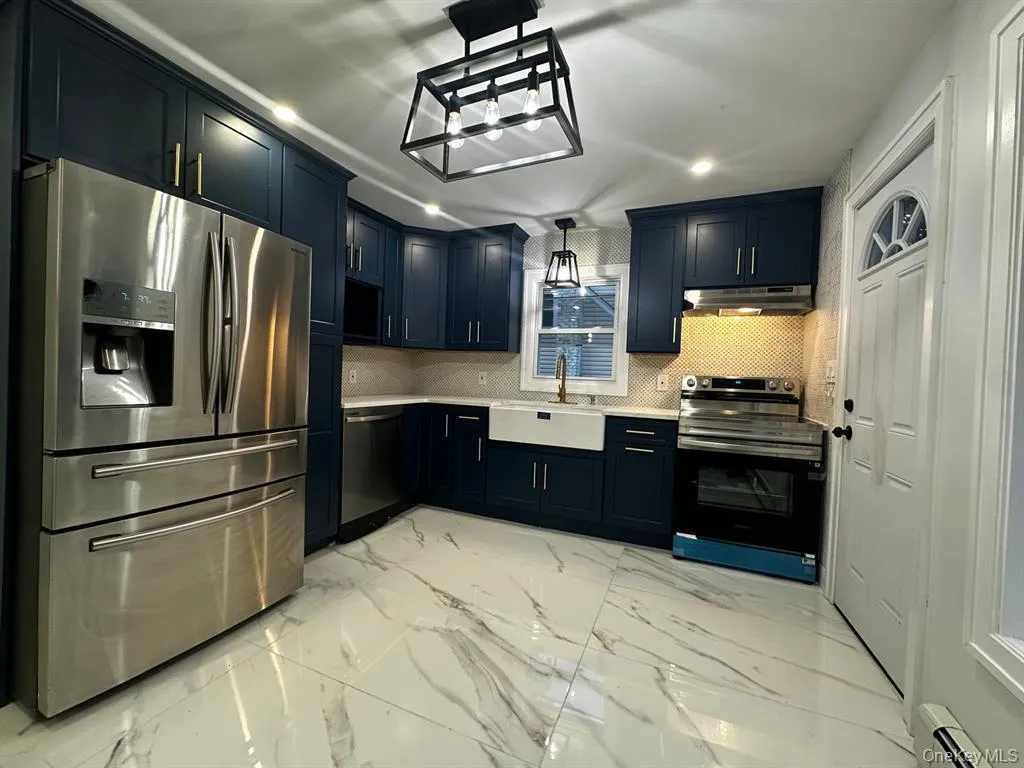 Kitchen with stainless steel appliances, light marble finish flooring, decorative light fixtures, baseboard heating, and backsplash Kitchen with stainless steel appliances, light marble finish flooring, decorative light fixtures, baseboard heating, and backsplash