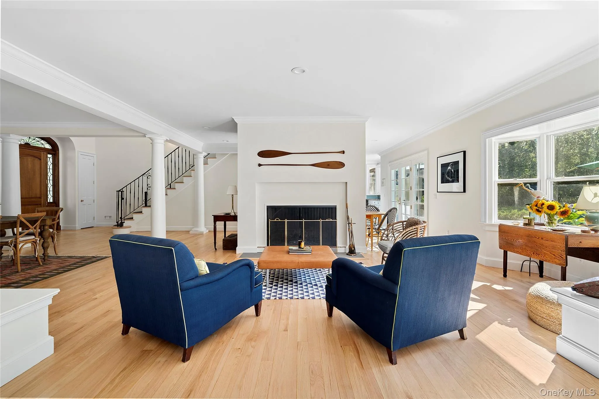 Living room featuring a fireplace, ornamental molding, light wood finished floors, stairway, and ornate columns Living room featuring a fireplace, ornamental molding, light wood finished floors, stairway, and ornate columns