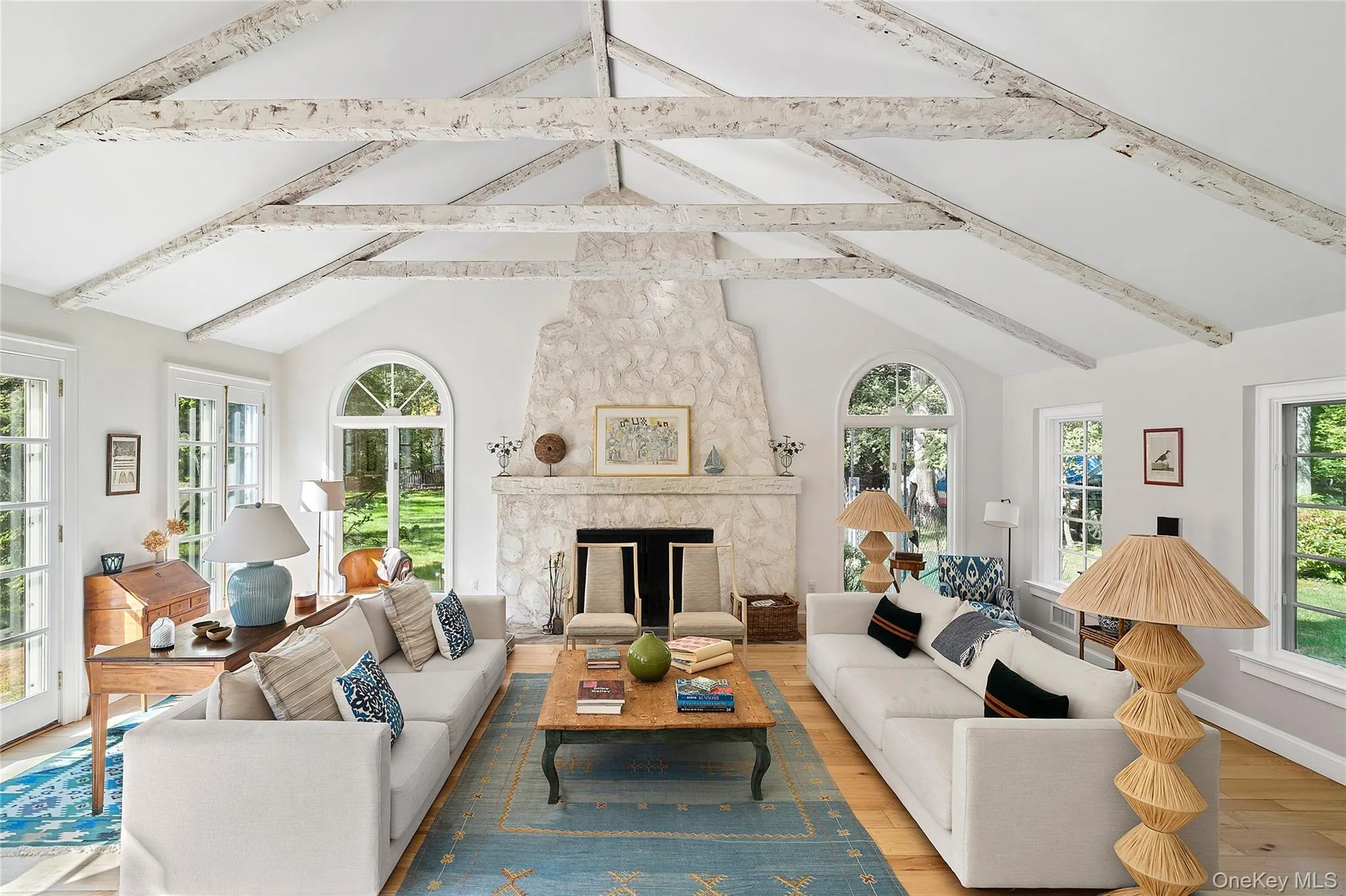 Living area featuring wood finished floors, a stone fireplace, high vaulted ceiling, and beamed ceiling Living area featuring wood finished floors, a stone fireplace, high vaulted ceiling, and beamed ceiling