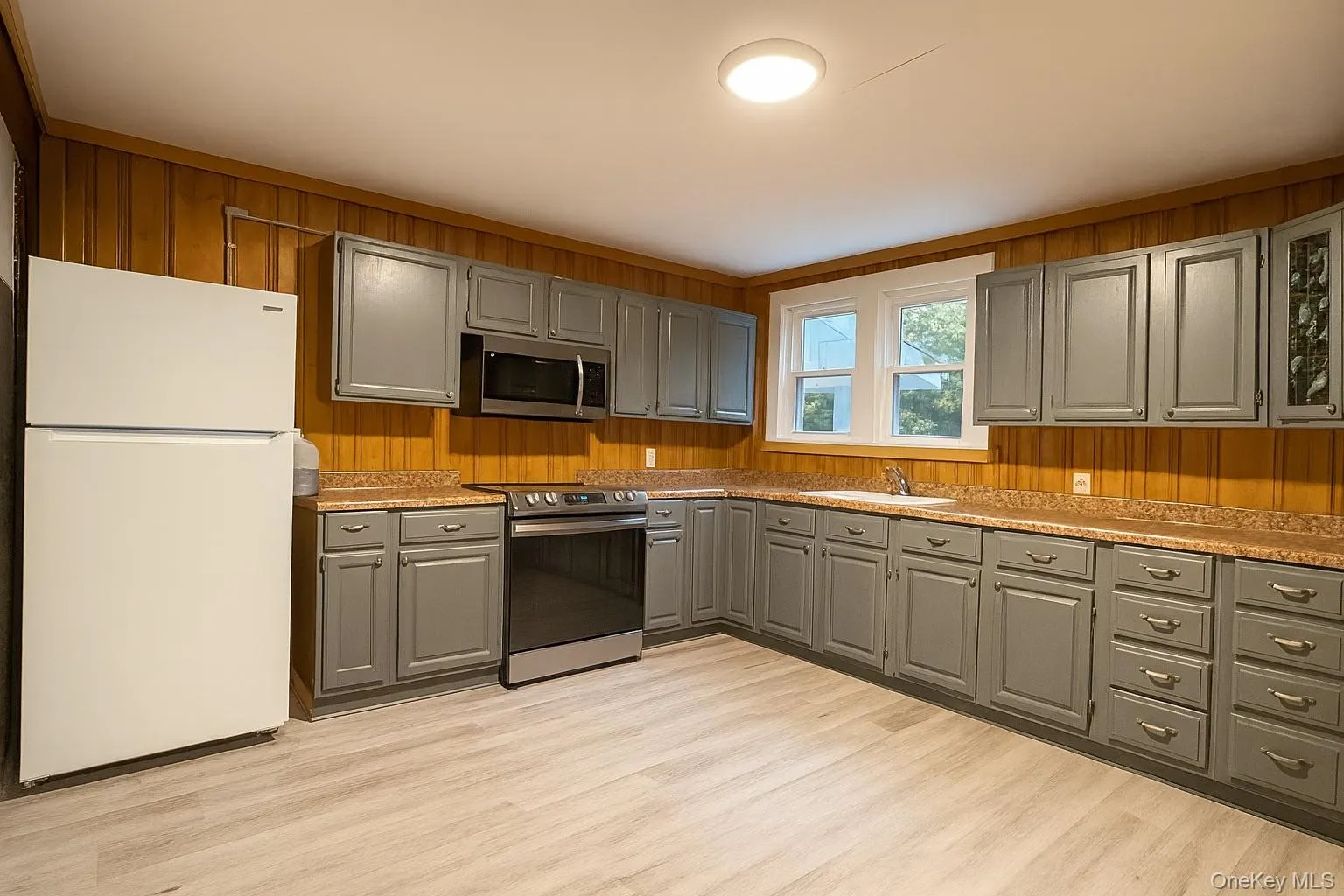 Kitchen featuring wood walls, gray cabinetry, stainless steel appliances, light countertops, and light wood-style flooring Kitchen featuring wood walls, gray cabinetry, stainless steel appliances, light countertops, and light wood-style flooring