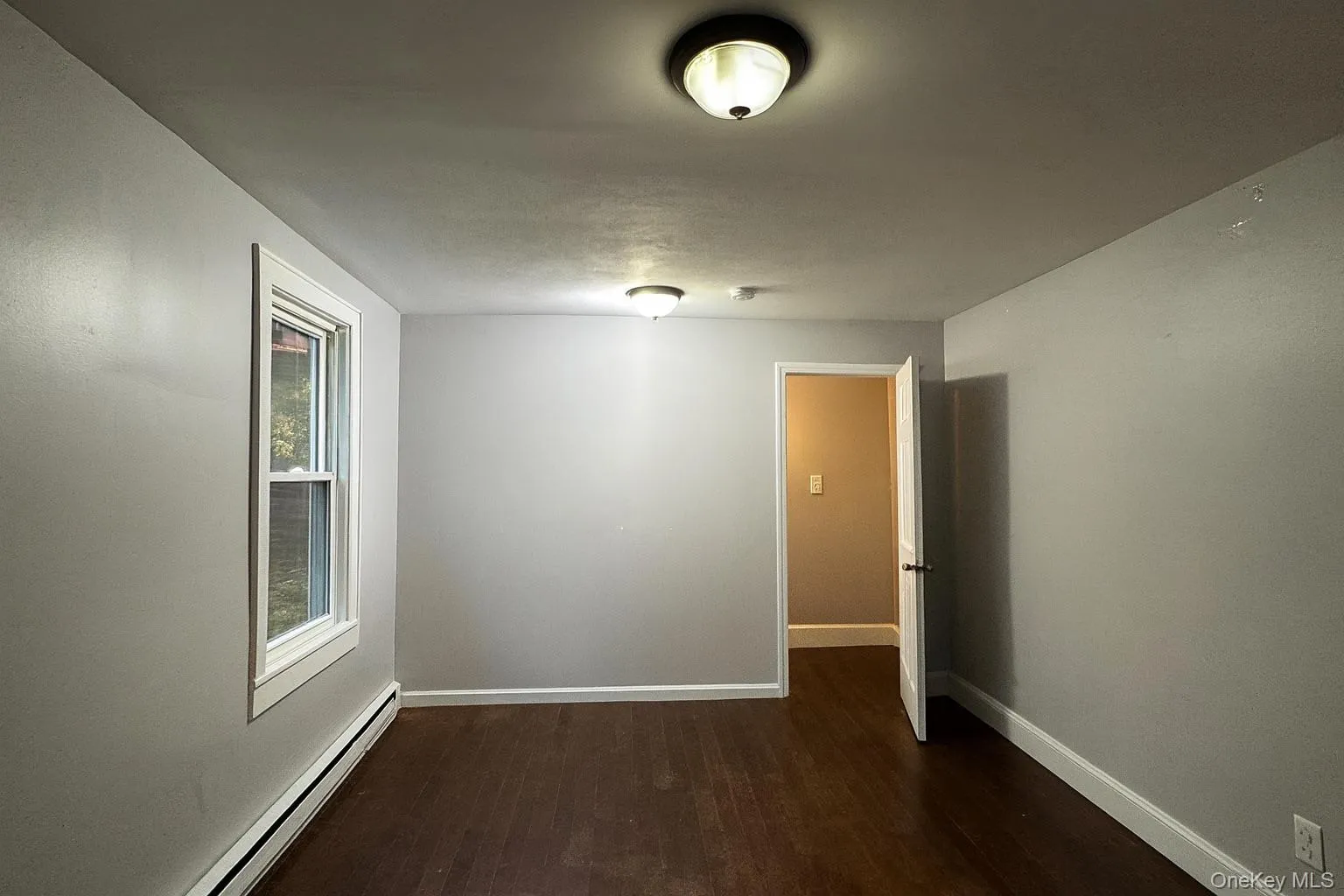 Unfurnished room featuring a baseboard heating unit and dark wood-style flooring Unfurnished room featuring a baseboard heating unit and dark wood-style flooring