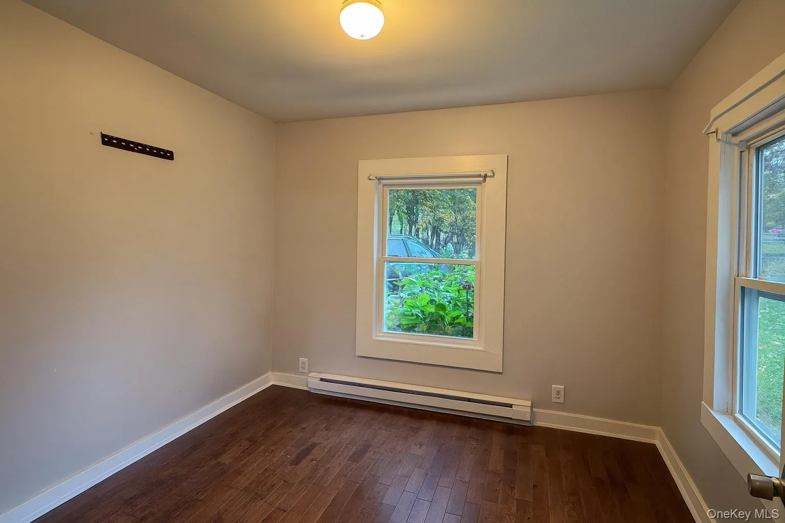 Unfurnished room featuring dark wood-style flooring and a baseboard radiator Unfurnished room featuring dark wood-style flooring and a baseboard radiator