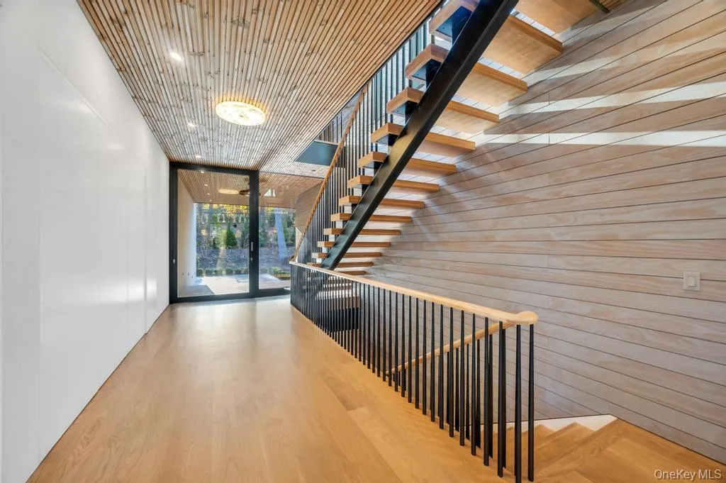 Hallway featuring stairway, wooden walls, wood finished floors, floor to ceiling windows, and an upstairs landing Hallway featuring stairway, wooden walls, wood finished floors, floor to ceiling windows, and an upstairs landing