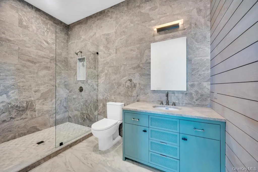 Bathroom with a walk in shower, tile walls, vanity, and light marble finish flooring Bathroom with a walk in shower, tile walls, vanity, and light marble finish flooring