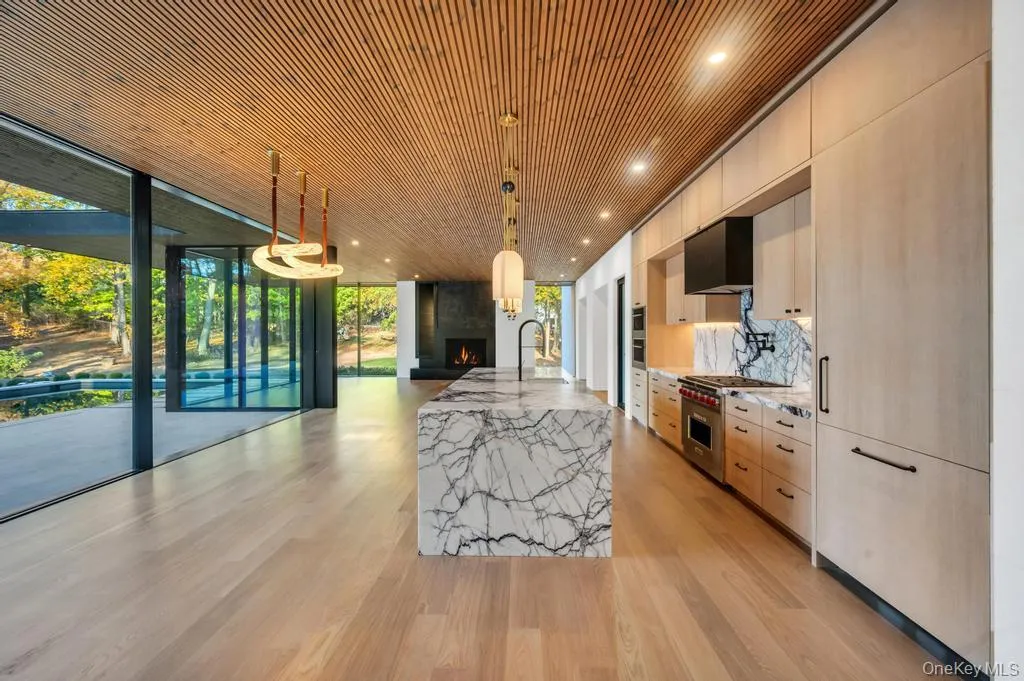 Kitchen featuring a wall of windows, decorative light fixtures, light stone countertops, a large island, and a fireplace Kitchen featuring a wall of windows, decorative light fixtures, light stone countertops, a large island, and a fireplace