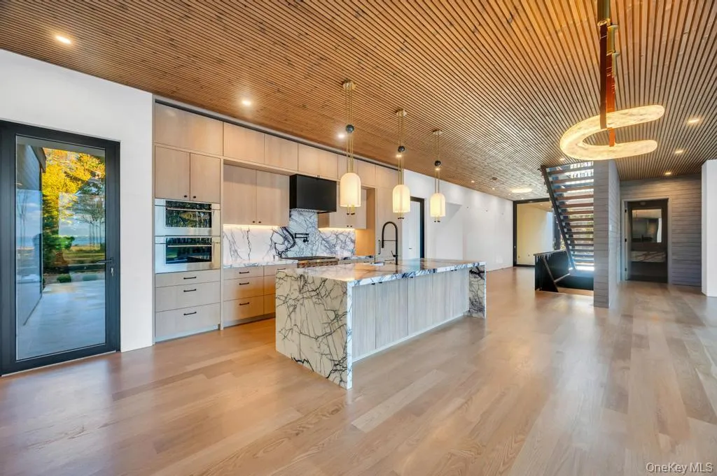Kitchen featuring hanging light fixtures, light brown cabinetry, light stone countertops, tasteful backsplash, and light wood finished floors Kitchen featuring hanging light fixtures, light brown cabinetry, light stone countertops, tasteful backsplash, and light wood finished floors