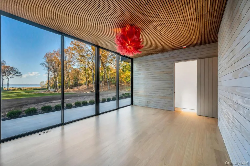 Empty room featuring floor to ceiling windows, wood walls, wood finished floors, and a water view Empty room featuring floor to ceiling windows, wood walls, wood finished floors, and a water view
