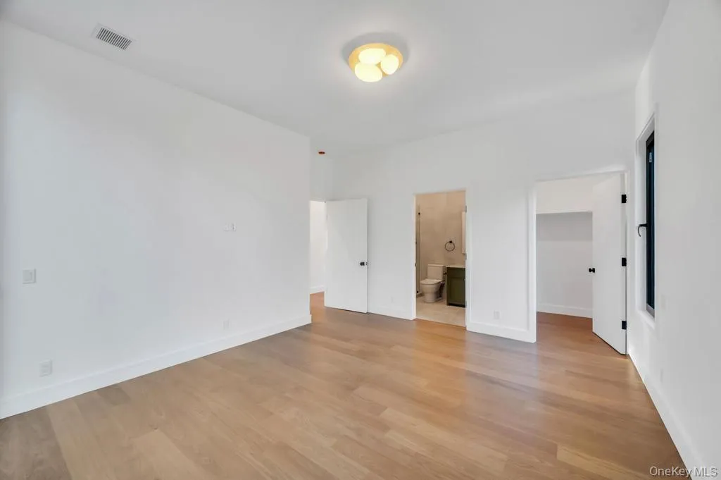Unfurnished bedroom with a spacious closet, light wood finished floors, and ensuite bathroom Unfurnished bedroom with a spacious closet, light wood finished floors, and ensuite bathroom