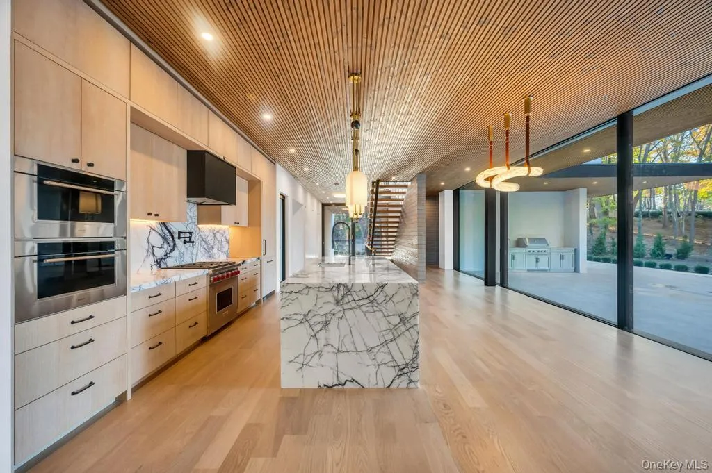 Kitchen with light brown cabinets, light stone counters, expansive windows, decorative light fixtures, and stainless steel appliances Kitchen with light brown cabinets, light stone counters, expansive windows, decorative light fixtures, and stainless steel appliances